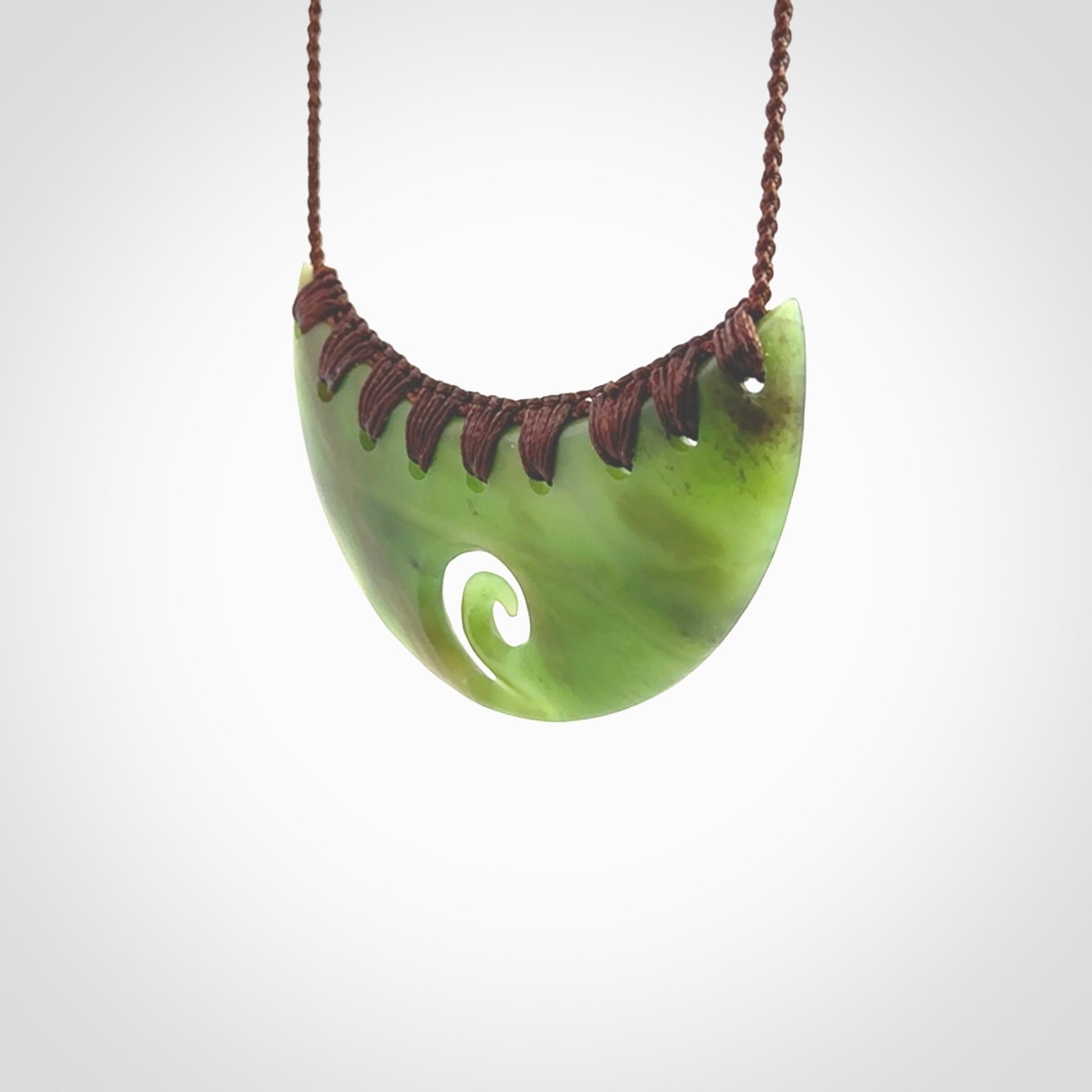 This picture shows a hand carved jade half-shield with Koru pendant. It is a semi-translucent green colour. This is a wonderful piece of jewellery. The cord is hand plaited and adjustable so that you can position the pendant where it suits you best. This piece was carved for us by Ric Moor. Delivery is free worldwide.