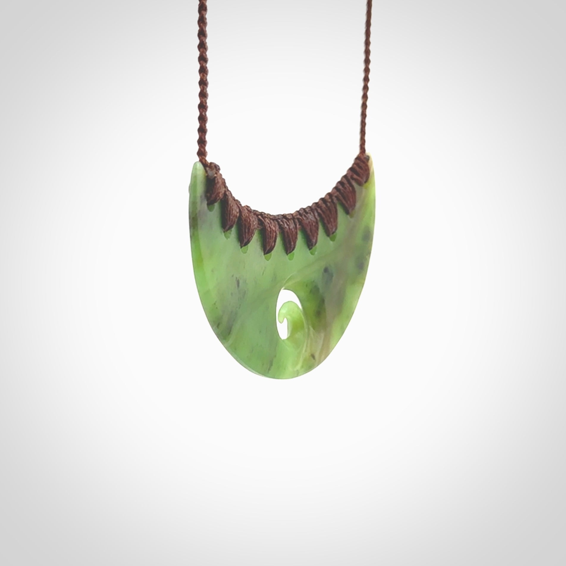 This picture shows a hand carved jade half-shield with Koru pendant. It is a semi-translucent green colour. This is a wonderful piece of jewellery. The cord is hand plaited and adjustable so that you can position the pendant where it suits you best. This piece was carved for us by Ric Moor. Delivery is free worldwide.