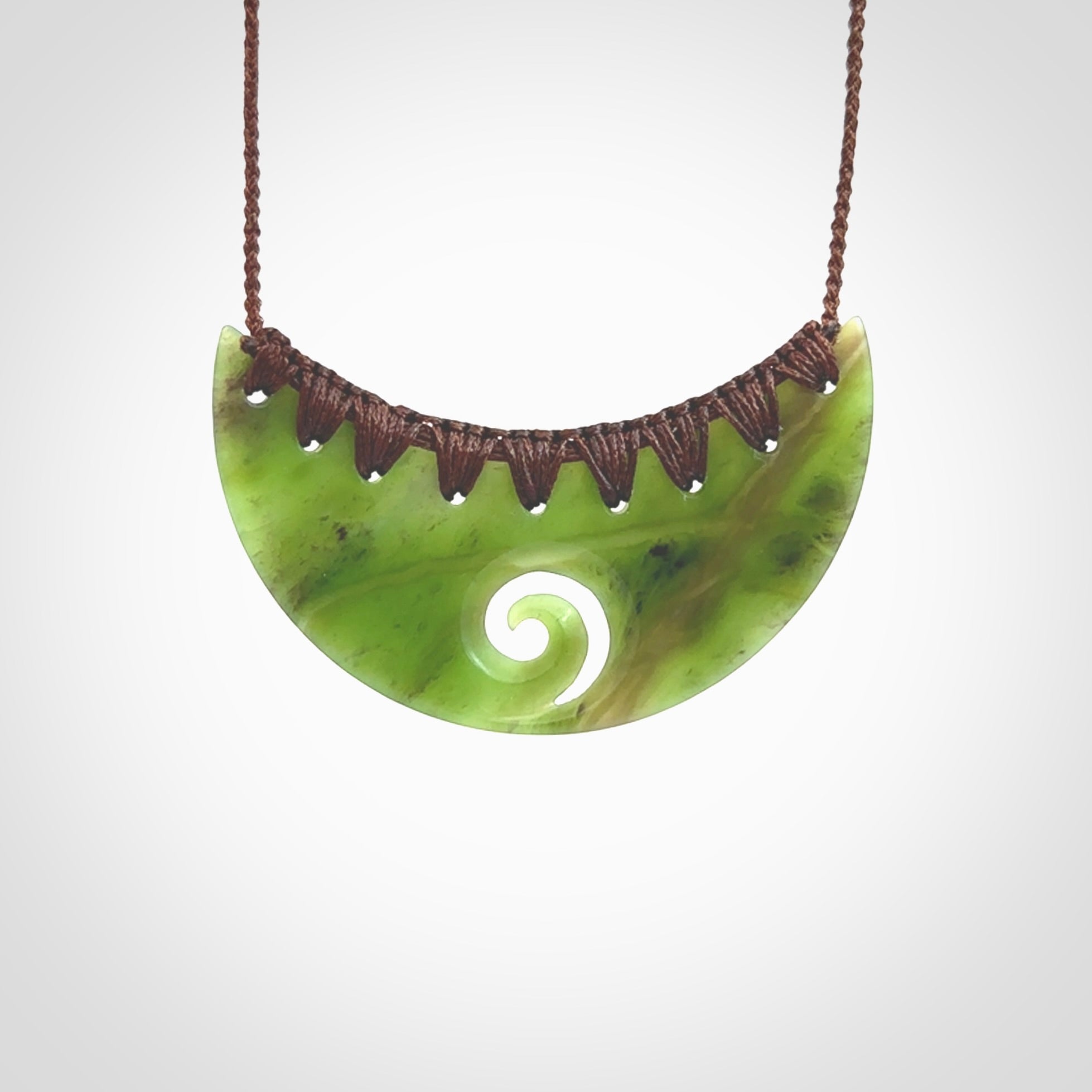 This picture shows a hand carved jade half-shield with Koru pendant. It is a semi-translucent green colour. This is a wonderful piece of jewellery. The cord is hand plaited and adjustable so that you can position the pendant where it suits you best. This piece was carved for us by Ric Moor. Delivery is free worldwide.