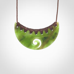 This picture shows a hand carved jade half-shield with Koru pendant. It is a semi-translucent green colour. This is a wonderful piece of jewellery. The cord is hand plaited and adjustable so that you can position the pendant where it suits you best. This piece was carved for us by Ric Moor. Delivery is free worldwide.