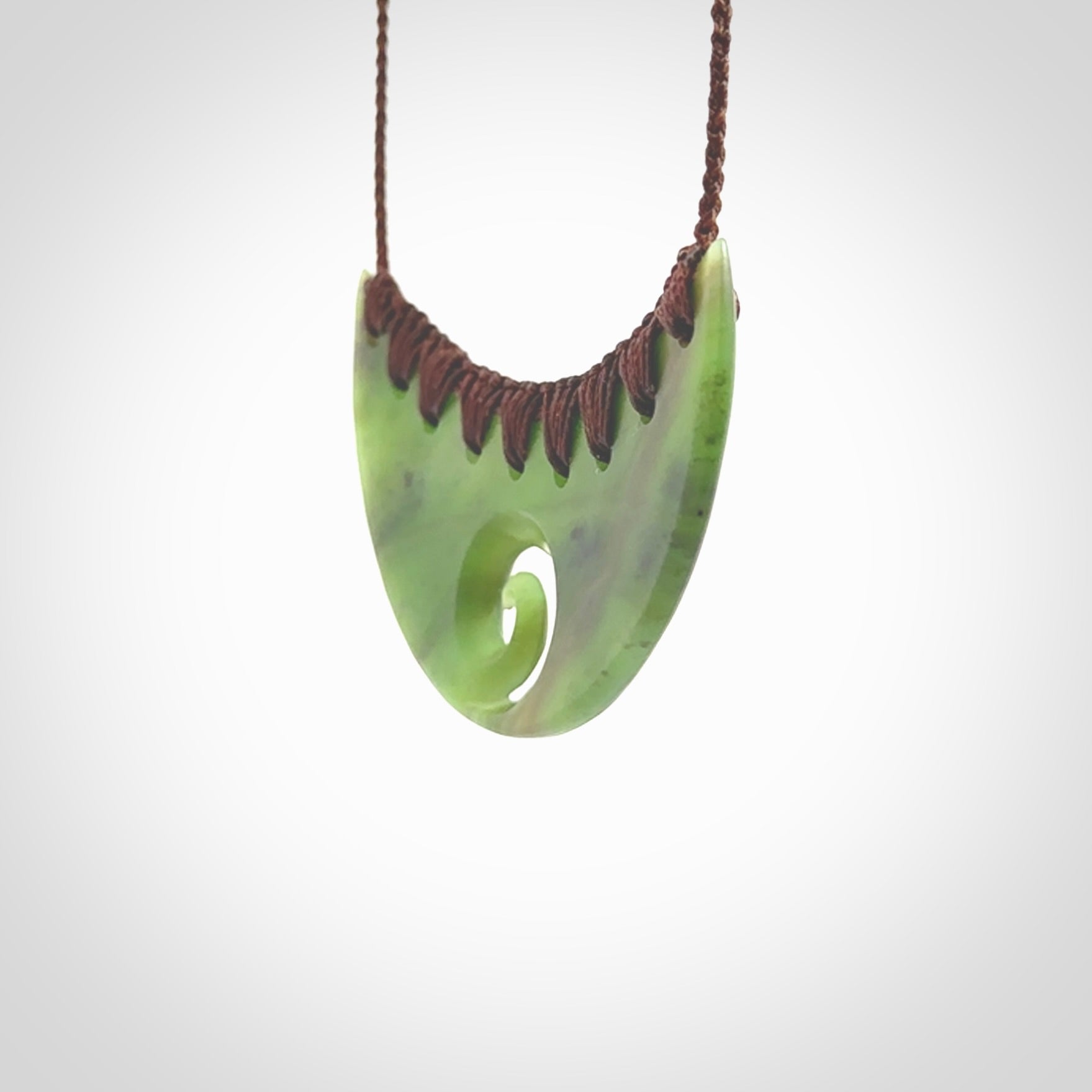 This picture shows a hand carved jade half-shield with Koru pendant. It is a semi-translucent green colour. This is a wonderful piece of jewellery. The cord is hand plaited and adjustable so that you can position the pendant where it suits you best. This piece was carved for us by Ric Moor. Delivery is free worldwide.