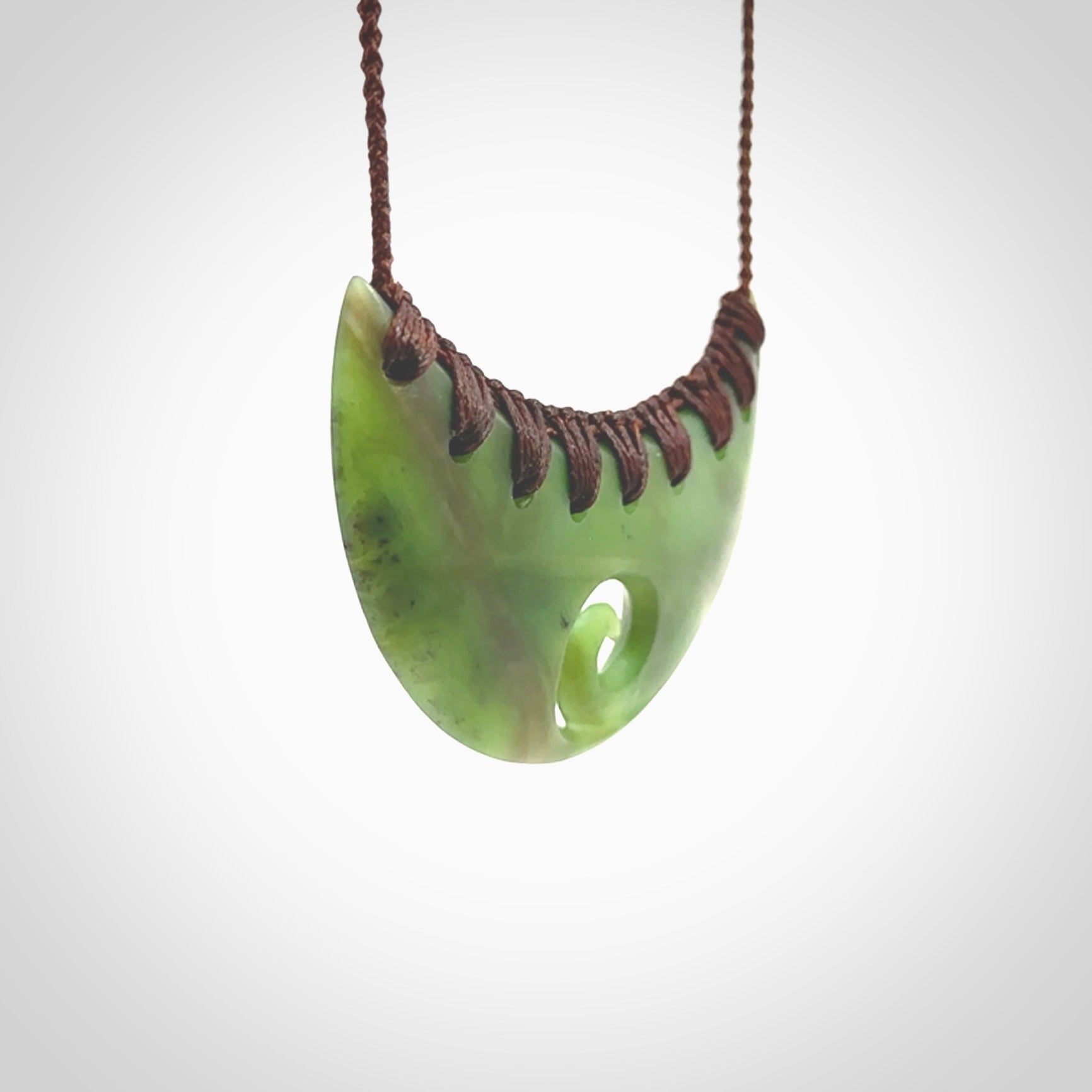 This picture shows a hand carved jade half-shield with Koru pendant. It is a semi-translucent green colour. This is a wonderful piece of jewellery. The cord is hand plaited and adjustable so that you can position the pendant where it suits you best. This piece was carved for us by Ric Moor. Delivery is free worldwide.