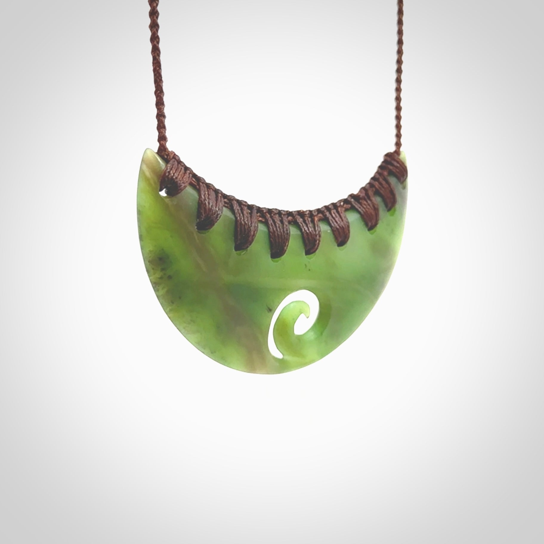 This picture shows a hand carved jade half-shield with Koru pendant. It is a semi-translucent green colour. This is a wonderful piece of jewellery. The cord is hand plaited and adjustable so that you can position the pendant where it suits you best. This piece was carved for us by Ric Moor. Delivery is free worldwide.