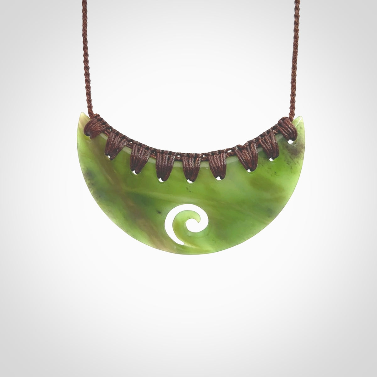 This picture shows a hand carved jade half-shield with Koru pendant. It is a semi-translucent green colour. This is a wonderful piece of jewellery. The cord is hand plaited and adjustable so that you can position the pendant where it suits you best. This piece was carved for us by Ric Moor. Delivery is free worldwide.