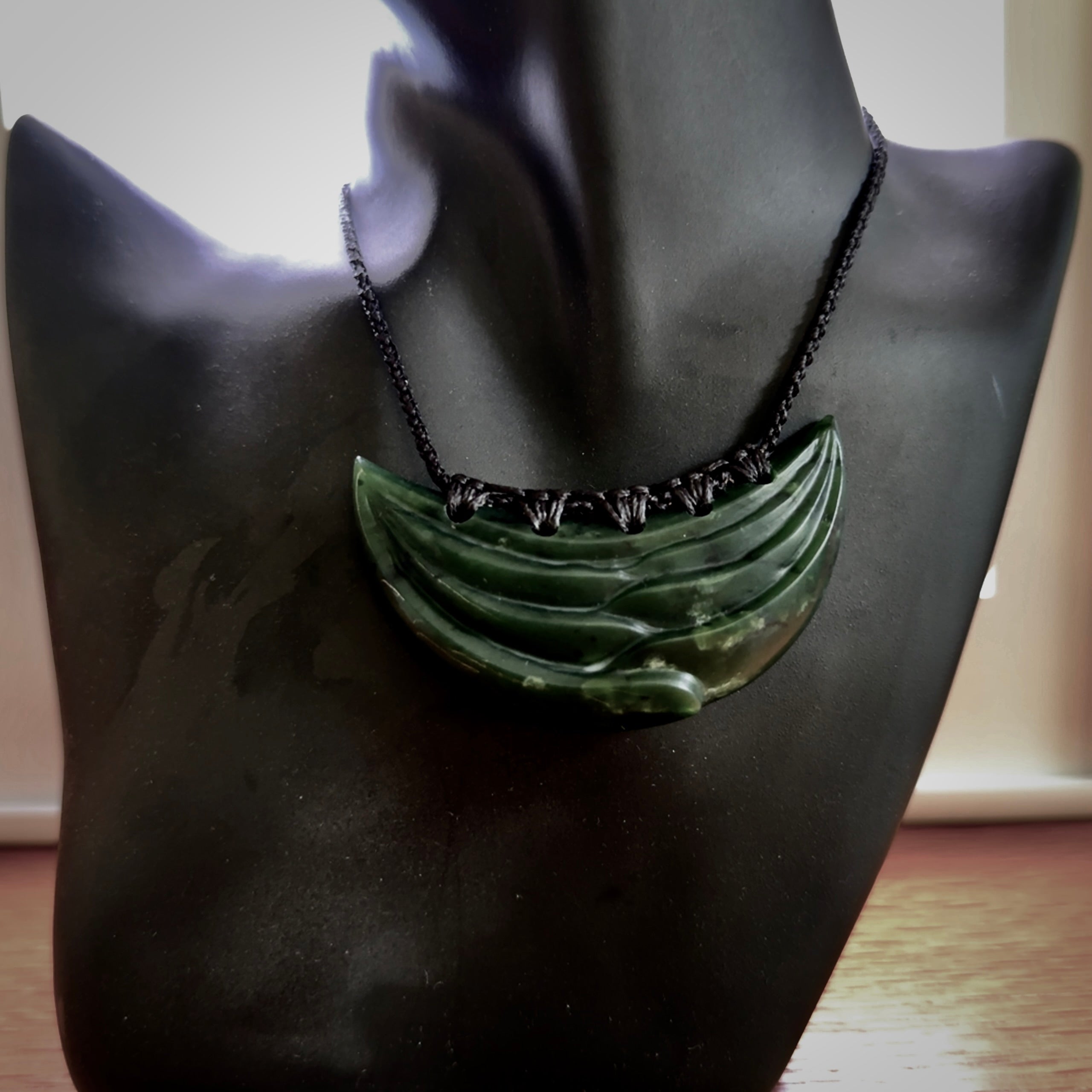 This picture shows a hand carved jade contemporary half-shield pendant. It is a deep green colour. This is a wonderful piece of jewellery. The cord is hand plaited and adjustable so that you can position the pendant where it suits you best. This piece was carved for us by Ric Moor. Delivery is free worldwide.