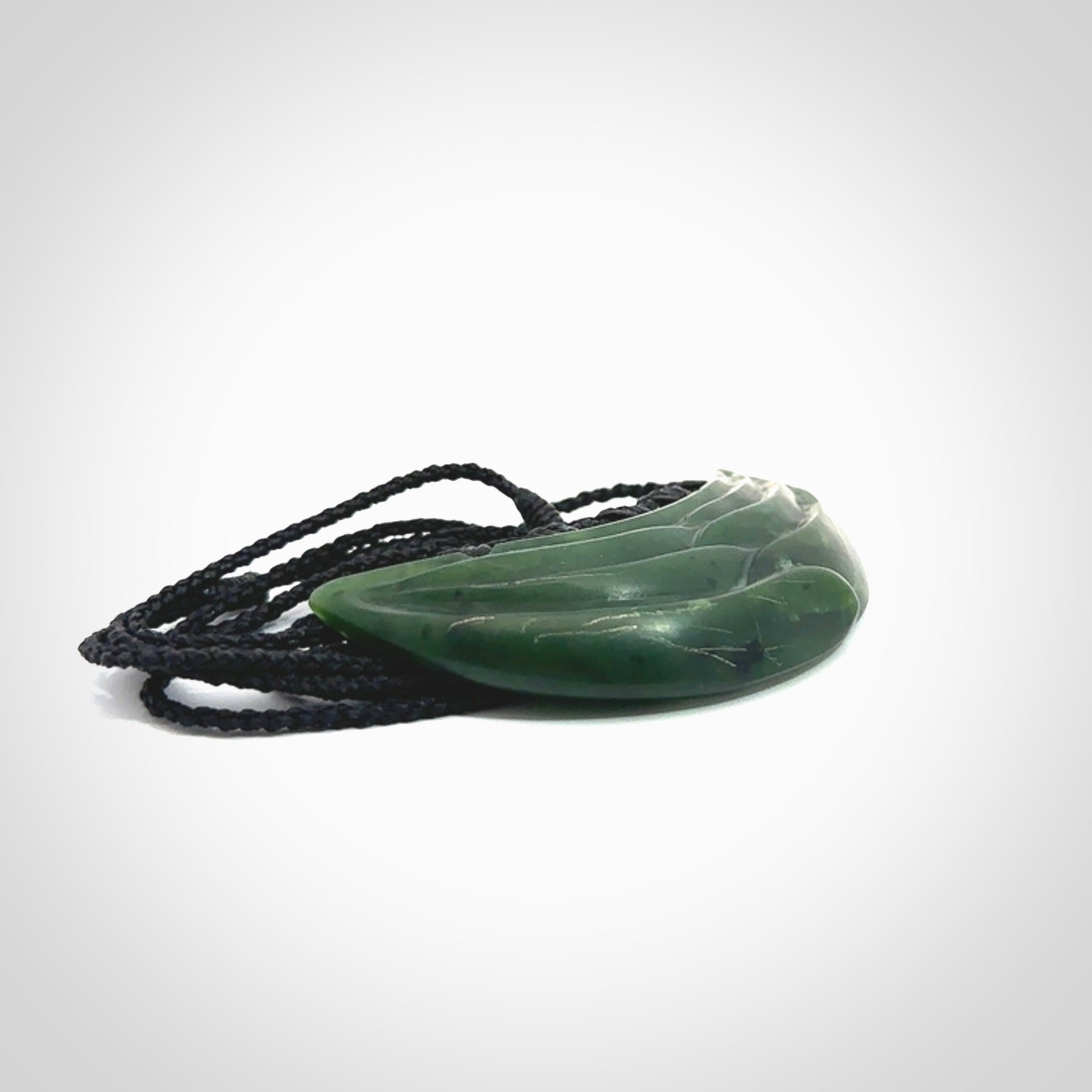 This picture shows a hand carved jade contemporary half-shield pendant. It is a deep green colour. This is a wonderful piece of jewellery. The cord is hand plaited and adjustable so that you can position the pendant where it suits you best. This piece was carved for us by Ric Moor. Delivery is free worldwide.