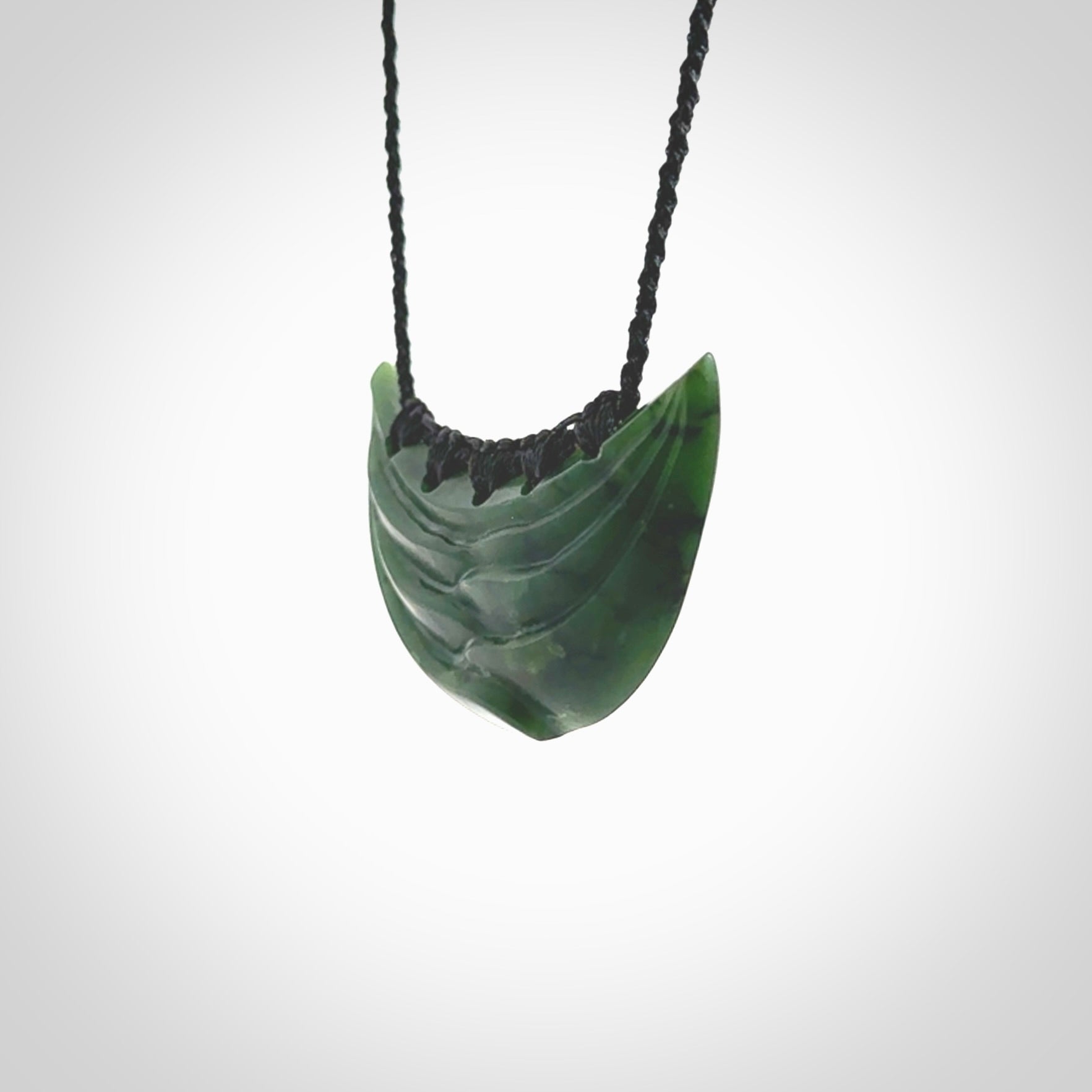 This picture shows a hand carved jade contemporary half-shield pendant. It is a deep green colour. This is a wonderful piece of jewellery. The cord is hand plaited and adjustable so that you can position the pendant where it suits you best. This piece was carved for us by Ric Moor. Delivery is free worldwide.