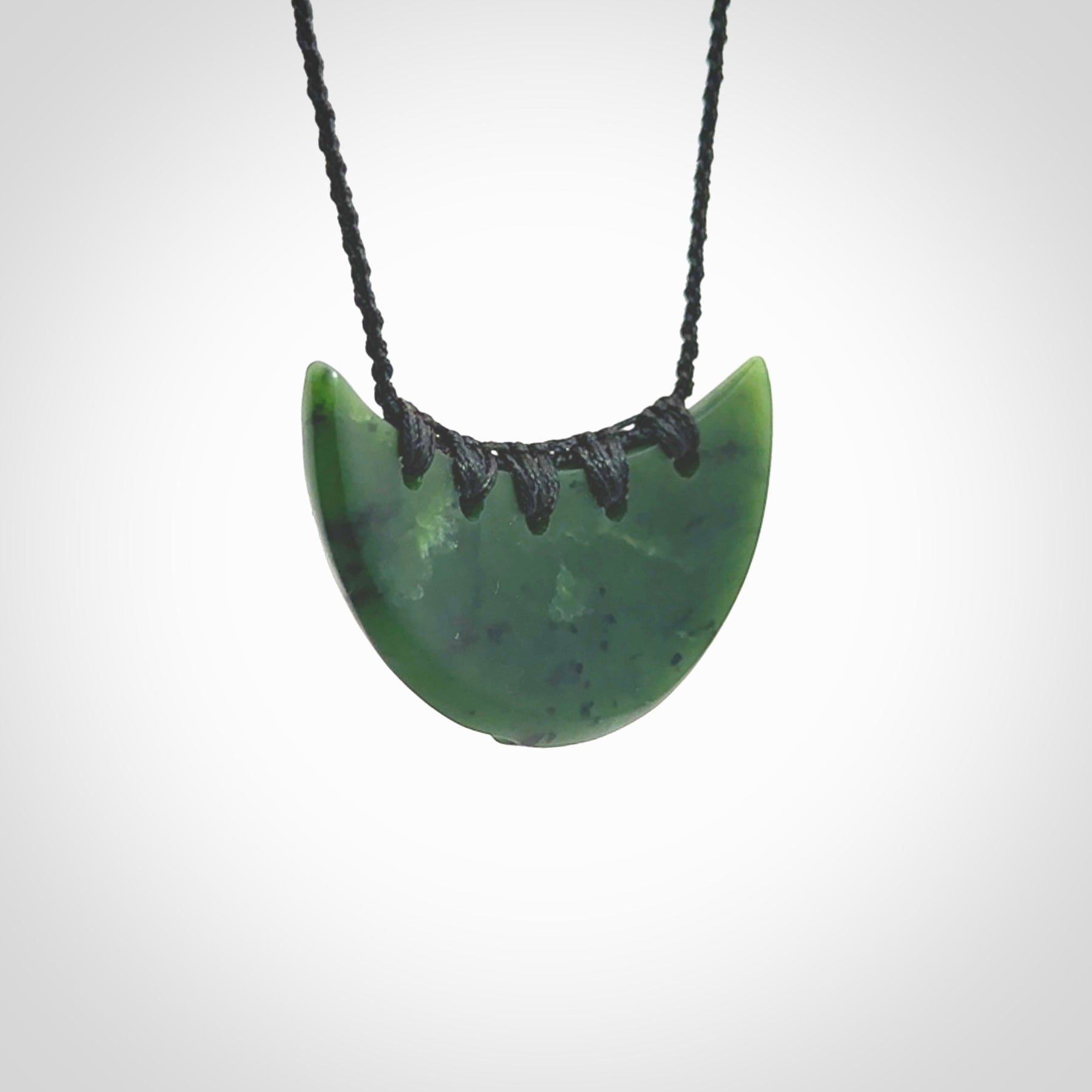 This picture shows a hand carved jade contemporary half-shield pendant. It is a deep green colour. This is a wonderful piece of jewellery. The cord is hand plaited and adjustable so that you can position the pendant where it suits you best. This piece was carved for us by Ric Moor. Delivery is free worldwide.