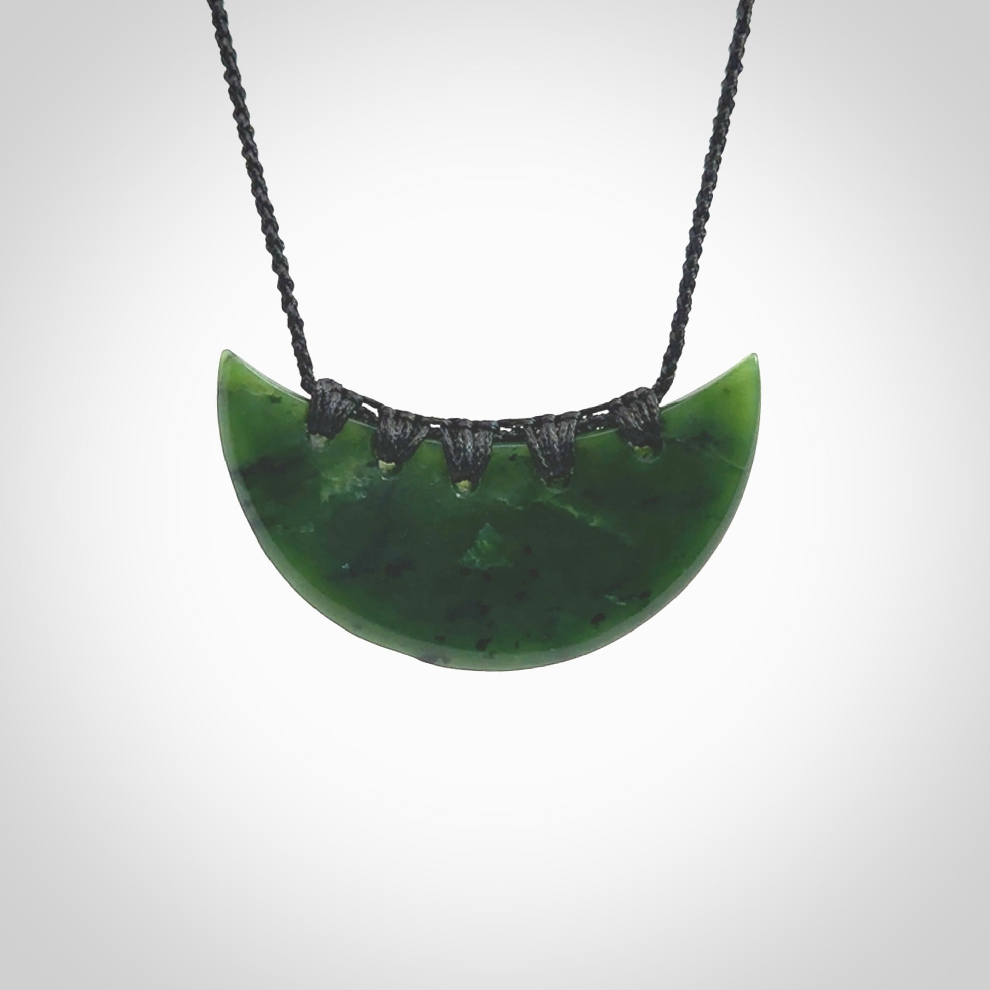 This picture shows a hand carved jade contemporary half-shield pendant. It is a deep green colour. This is a wonderful piece of jewellery. The cord is hand plaited and adjustable so that you can position the pendant where it suits you best. This piece was carved for us by Ric Moor. Delivery is free worldwide.