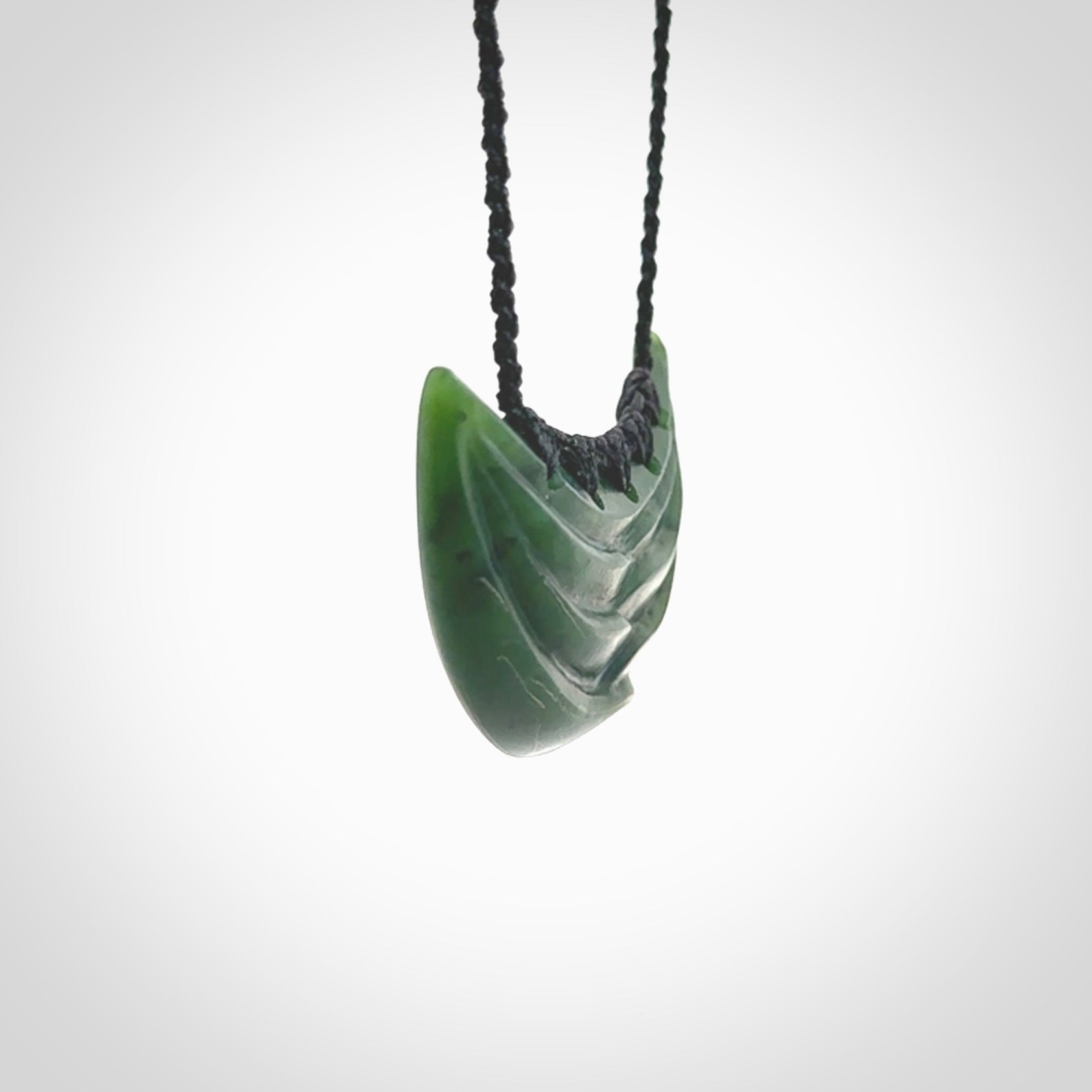 This picture shows a hand carved jade contemporary half-shield pendant. It is a deep green colour. This is a wonderful piece of jewellery. The cord is hand plaited and adjustable so that you can position the pendant where it suits you best. This piece was carved for us by Ric Moor. Delivery is free worldwide.