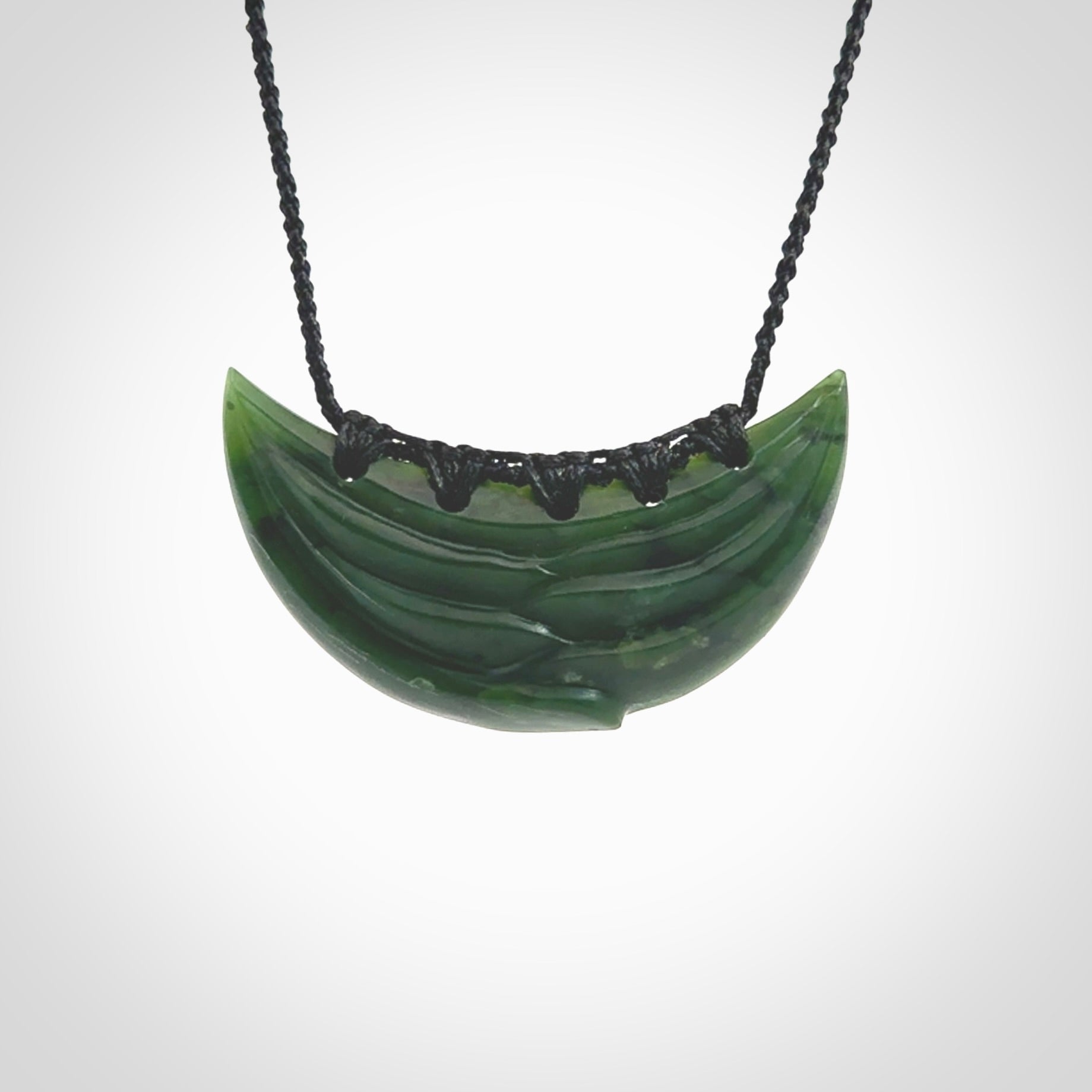 This picture shows a hand carved jade contemporary half-shield pendant. It is a deep green colour. This is a wonderful piece of jewellery. The cord is hand plaited and adjustable so that you can position the pendant where it suits you best. This piece was carved for us by Ric Moor. Delivery is free worldwide.