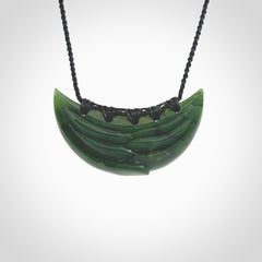 This picture shows a hand carved jade contemporary half-shield pendant. It is a deep green colour. This is a wonderful piece of jewellery. The cord is hand plaited and adjustable so that you can position the pendant where it suits you best. This piece was carved for us by Ric Moor. Delivery is free worldwide.