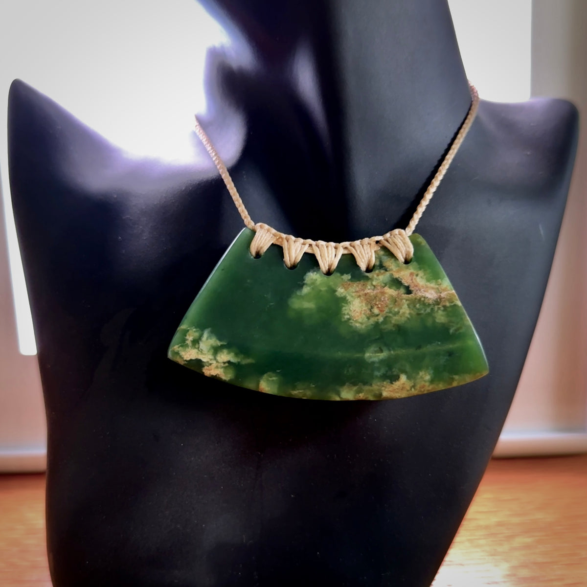 This picture shows a hand carved jade contemporary half-shield pendant. It is a deep green colour with orange and lighter shades of green throughout. This is a wonderful piece of jewellery. The cord is hand plaited and adjustable so that you can position the pendant where it suits you best. This piece was carved for us by Ric Moor. Delivery is free worldwide.