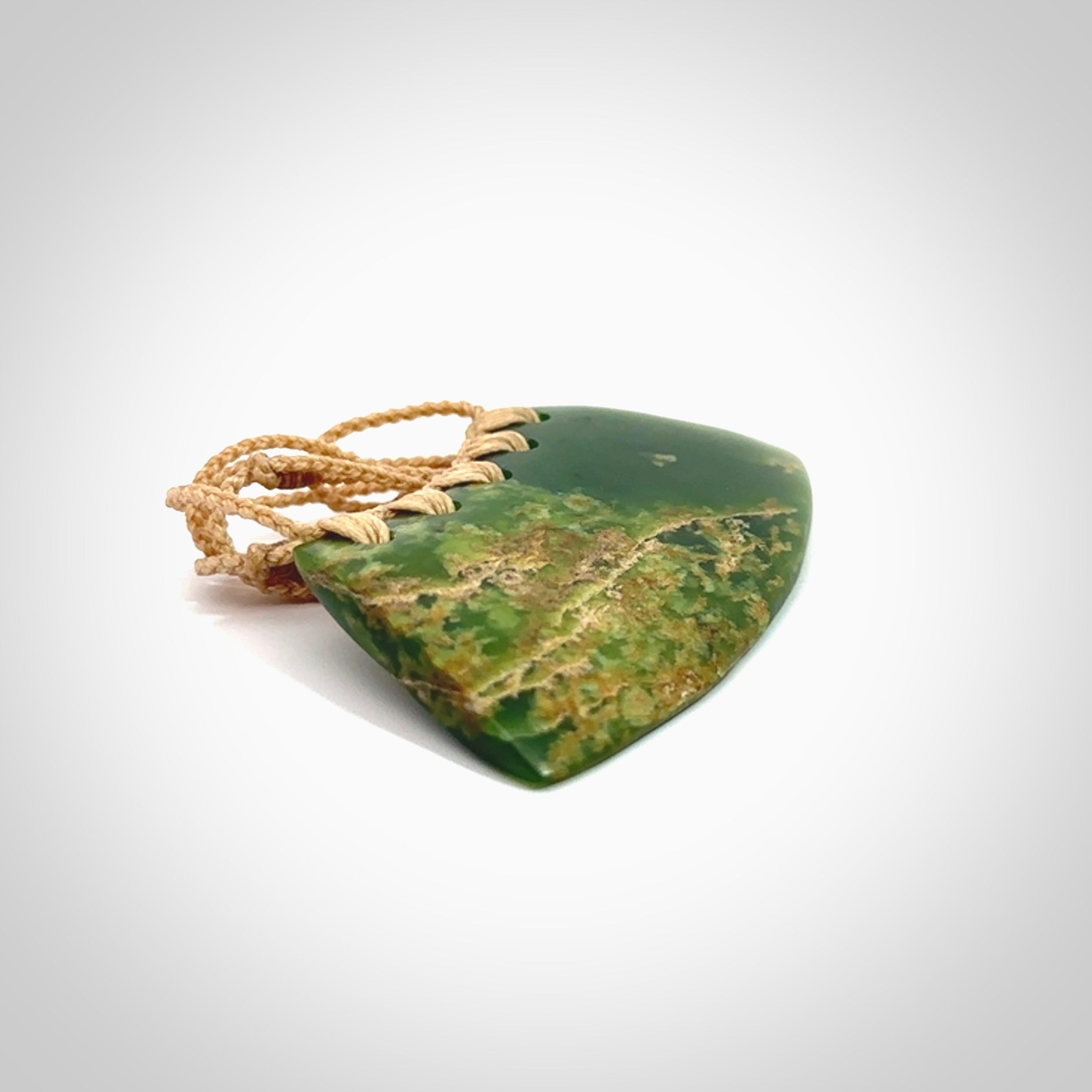 This picture shows a hand carved jade contemporary half-shield pendant. It is a deep green colour with orange and lighter shades of green throughout. This is a wonderful piece of jewellery. The cord is hand plaited and adjustable so that you can position the pendant where it suits you best. This piece was carved for us by Ric Moor. Delivery is free worldwide.