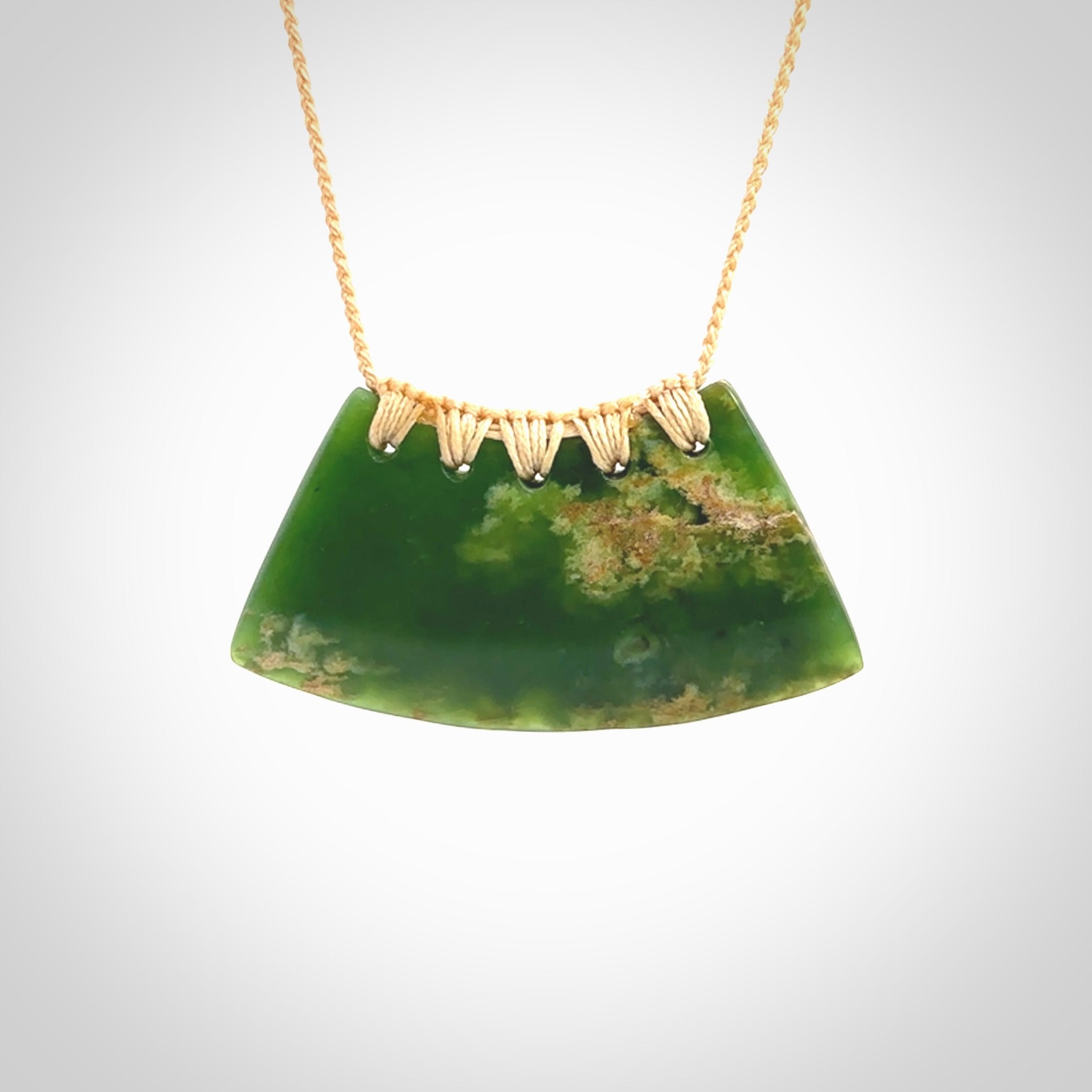 This picture shows a hand carved jade contemporary half-shield pendant. It is a deep green colour with orange and lighter shades of green throughout. This is a wonderful piece of jewellery. The cord is hand plaited and adjustable so that you can position the pendant where it suits you best. This piece was carved for us by Ric Moor. Delivery is free worldwide.