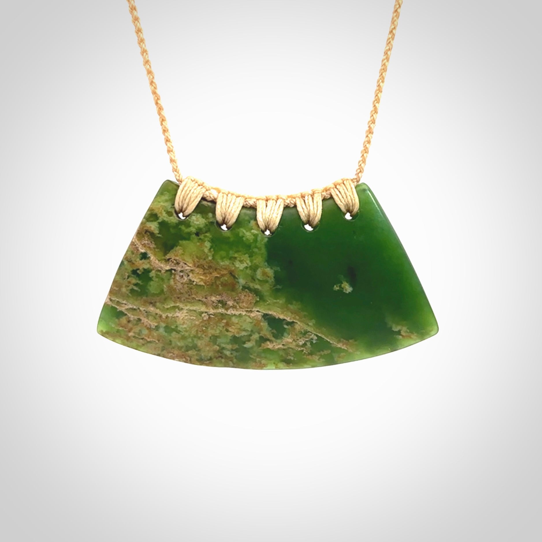 This picture shows a hand carved jade contemporary half-shield pendant. It is a deep green colour with orange and lighter shades of green throughout. This is a wonderful piece of jewellery. The cord is hand plaited and adjustable so that you can position the pendant where it suits you best. This piece was carved for us by Ric Moor. Delivery is free worldwide.