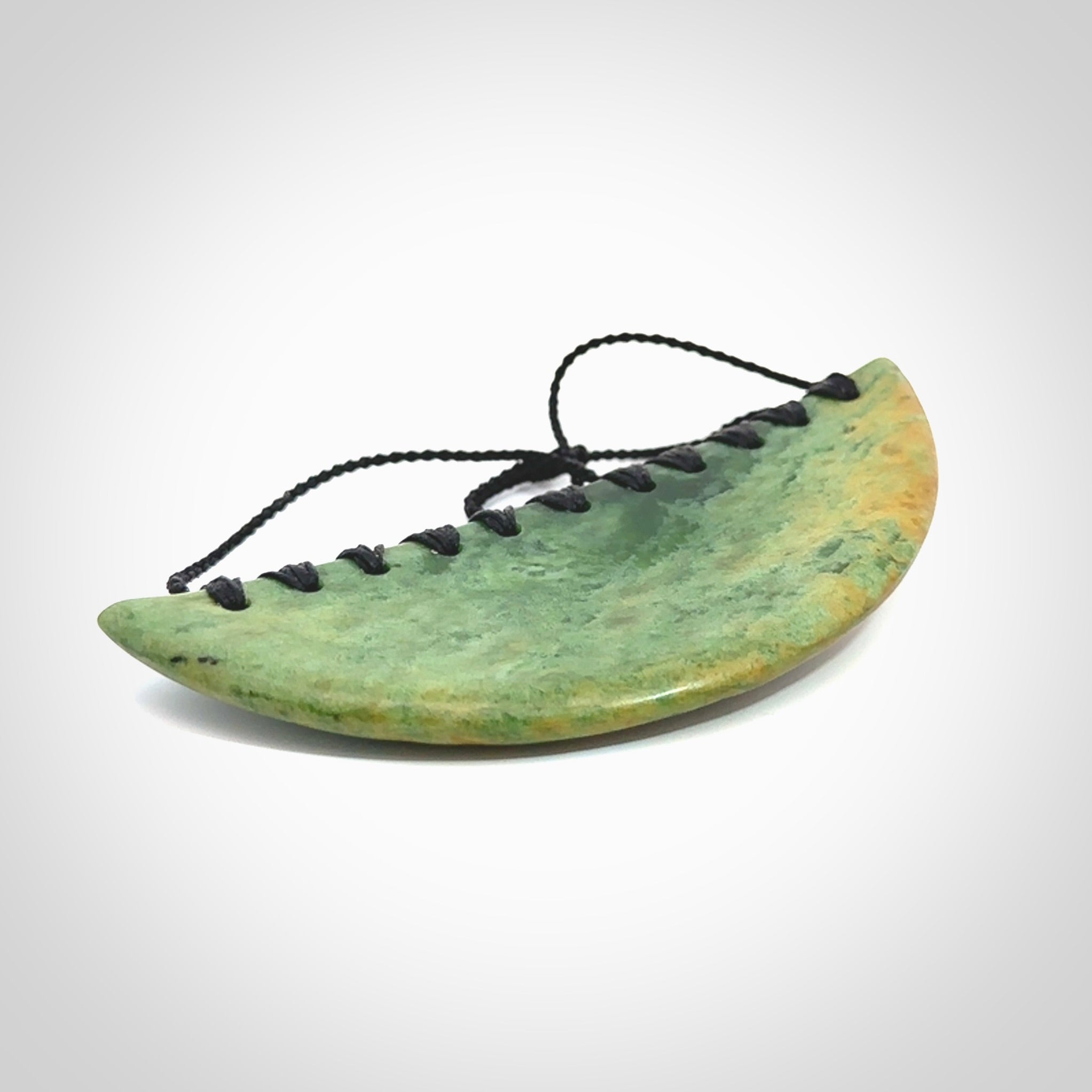 This picture shows a hand carved jade contemporary half-shield pendant. It is a light, minty green colour with orange shades and darker inclusions throughout. This is a wonderful piece of jewellery. The cord is hand plaited and adjustable so that you can position the pendant where it suits you best. This piece was carved for us by Ric Moor. Delivery is free worldwide.