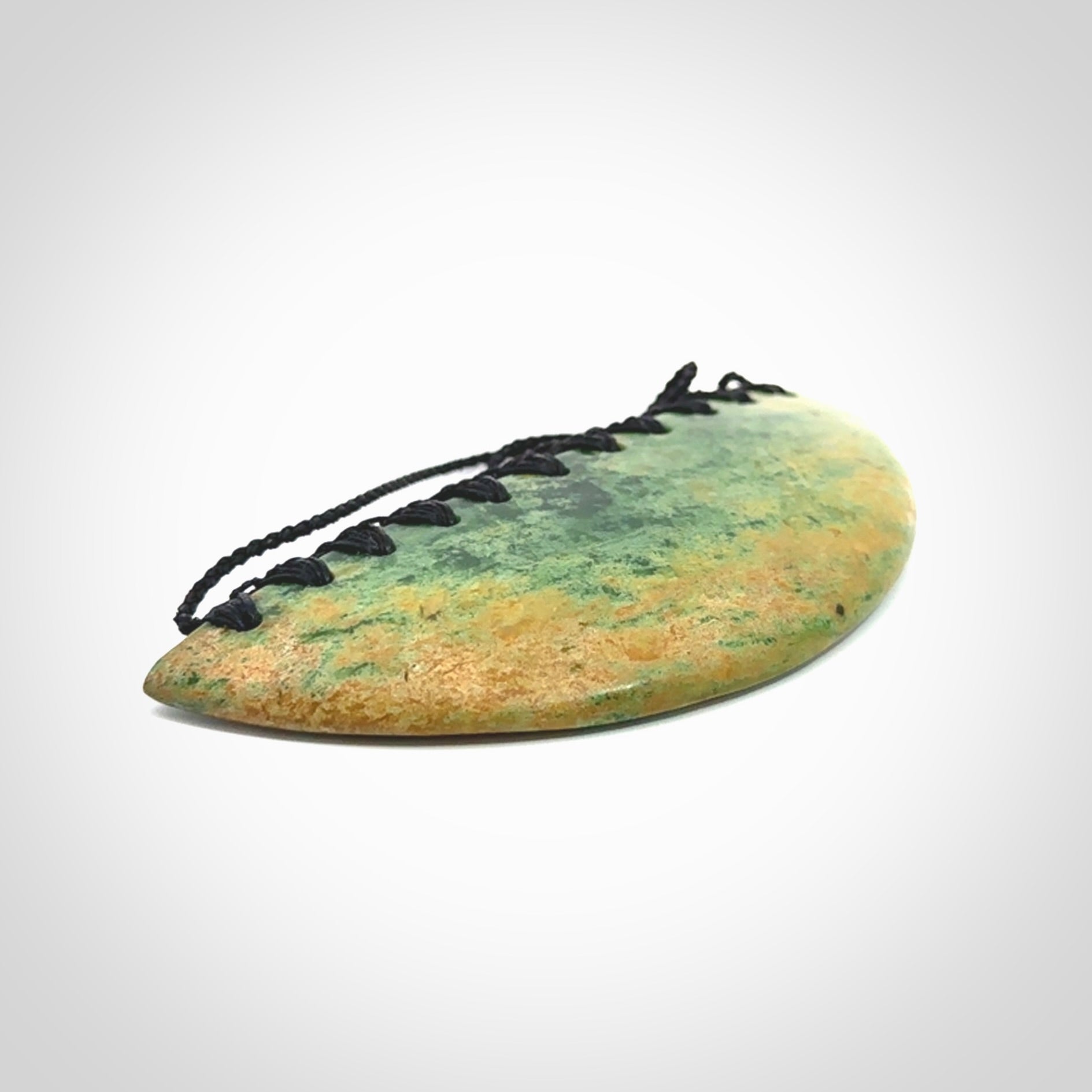 This picture shows a hand carved jade contemporary half-shield pendant. It is a light, minty green colour with orange shades and darker inclusions throughout. This is a wonderful piece of jewellery. The cord is hand plaited and adjustable so that you can position the pendant where it suits you best. This piece was carved for us by Ric Moor. Delivery is free worldwide.