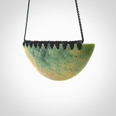 This picture shows a hand carved jade contemporary half-shield pendant. It is a light, minty green colour with orange shades and darker inclusions throughout. This is a wonderful piece of jewellery. The cord is hand plaited and adjustable so that you can position the pendant where it suits you best. This piece was carved for us by Ric Moor. Delivery is free worldwide.