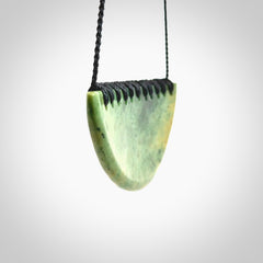 This picture shows a hand carved jade contemporary half-shield pendant. It is a light, minty green colour with orange shades and darker inclusions throughout. This is a wonderful piece of jewellery. The cord is hand plaited and adjustable so that you can position the pendant where it suits you best. This piece was carved for us by Ric Moor. Delivery is free worldwide.