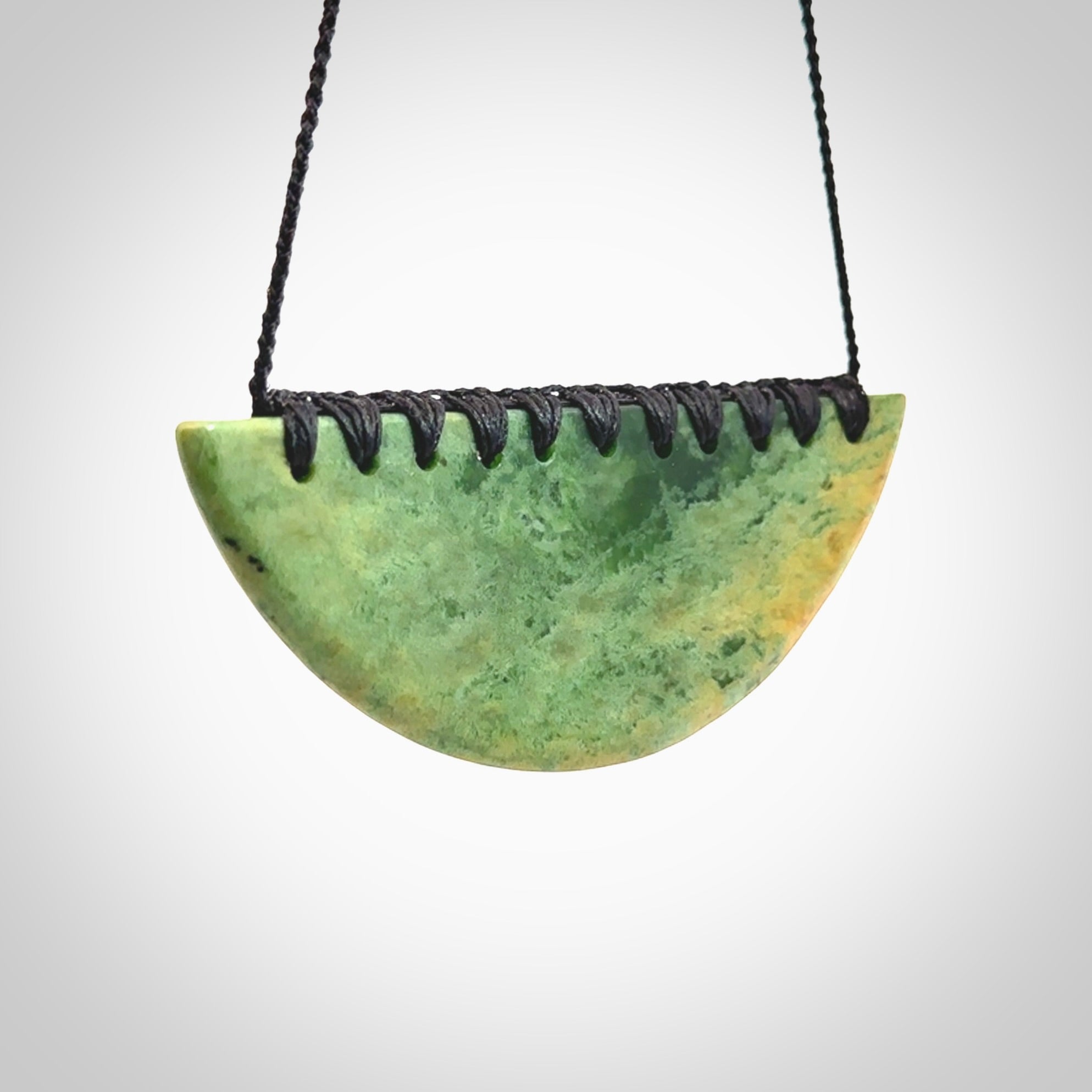 This picture shows a hand carved jade contemporary half-shield pendant. It is a light, minty green colour with orange shades and darker inclusions throughout. This is a wonderful piece of jewellery. The cord is hand plaited and adjustable so that you can position the pendant where it suits you best. This piece was carved for us by Ric Moor. Delivery is free worldwide.