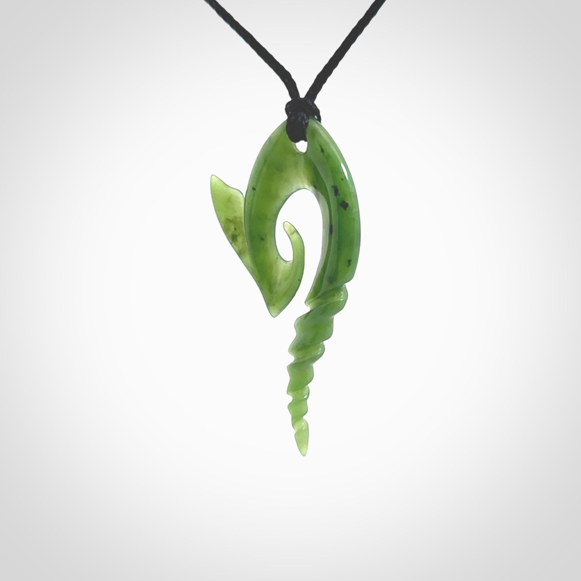 This photo shows a contemporary koru with whale tail pendant carved from New Zealand Jade. The artist, Shaun Gardiner, has carved this beautifully. We provide this piece with an adjustable Black cord. This is a fantastic work of art, we have one only.