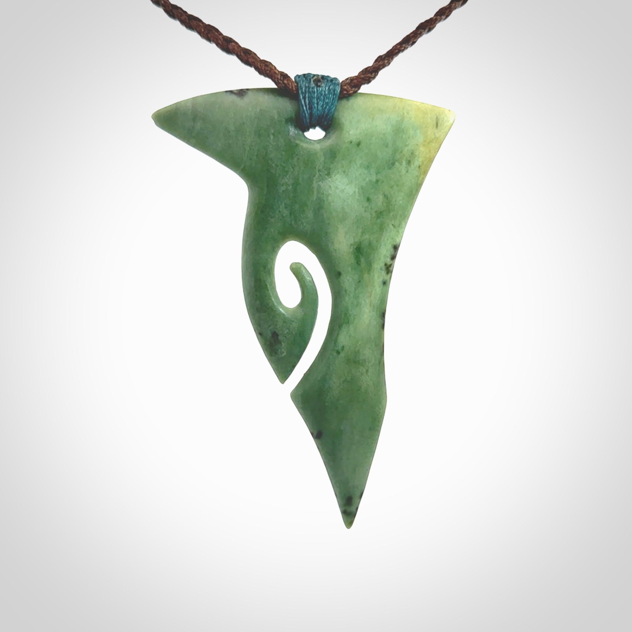 This photo shows a large shield with koru carved into New Zealand Kokopu Jade. The artist, Shaun Gardiner, has carved this beautifully. We have added a Sea Moss Blue ridge-top binding with adjustable Thick Brown cord. This is a fantastic work of art, we have one only.