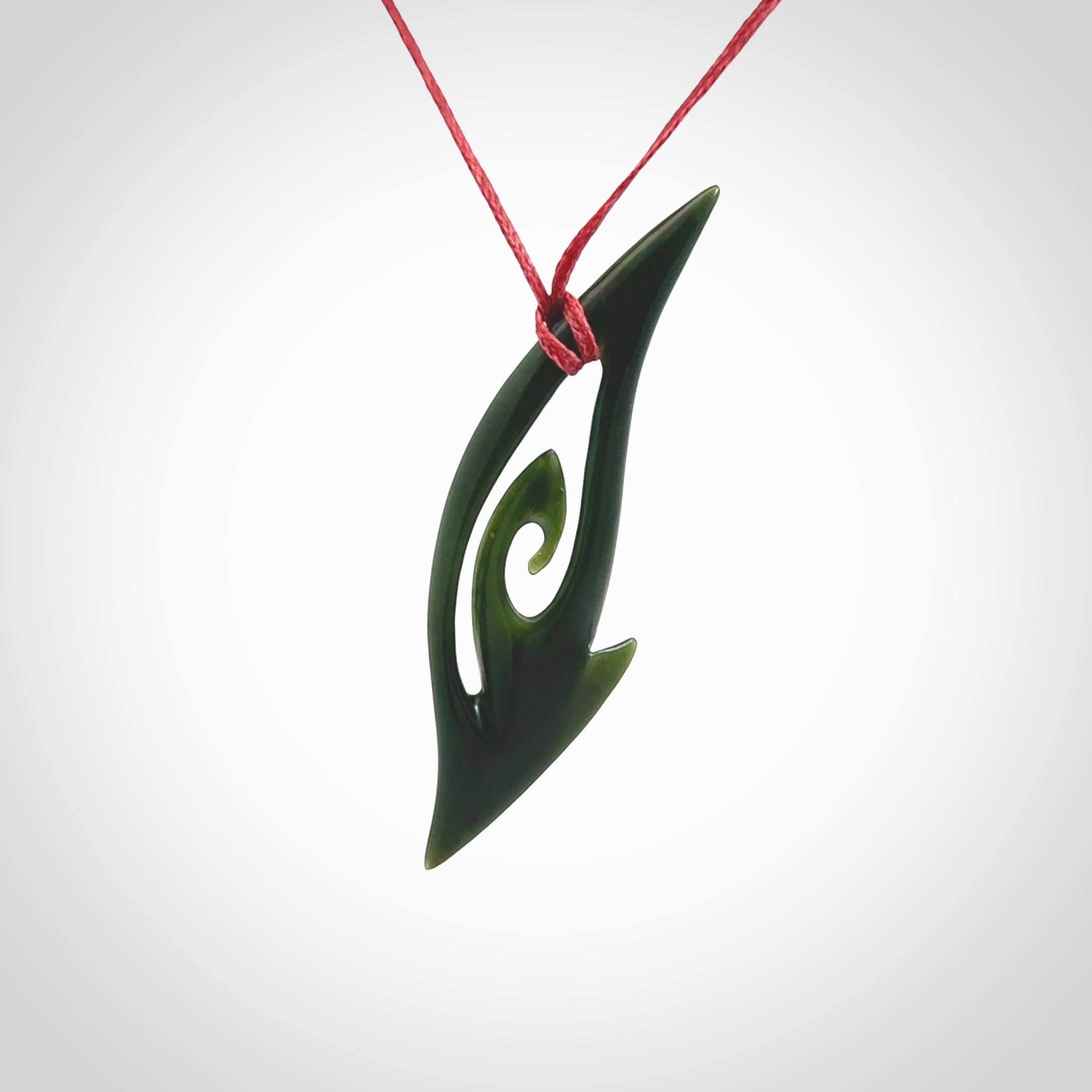 This photo shows a koru pendant carved from New Zealand Jade. The artist, Shaun Gardiner, has carved this beautifully. We provide this piece with an adjustable red cord. This is a fantastic work of art, we have one only.