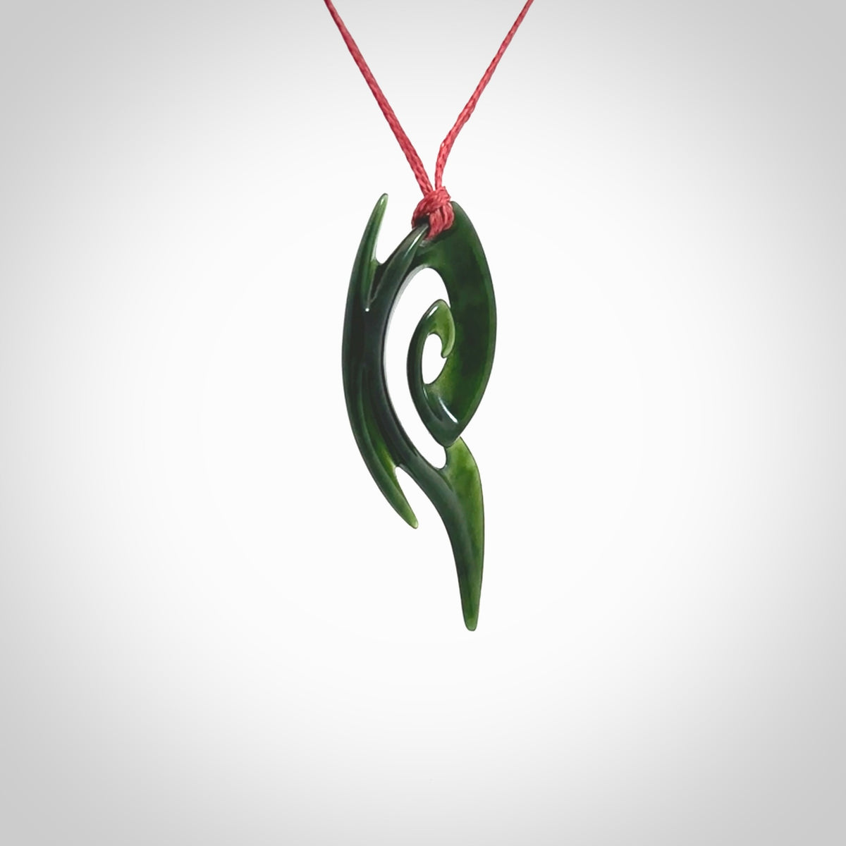 This photo shows a koru pendant carved from New Zealand Jade. The artist, Shaun Gardiner, has carved this beautifully. We provide this piece with an adjustable red cord. This is a fantastic work of art, we have one only.