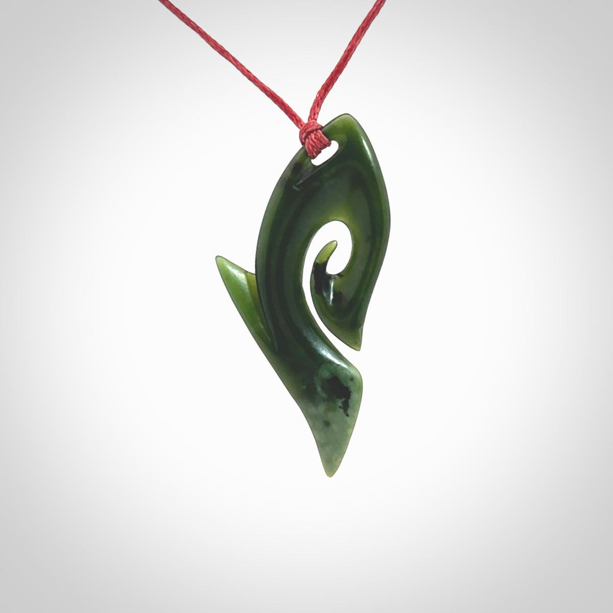 This photo shows a koru pendant carved from New Zealand Jade. The artist, Shaun Gardiner, has carved this beautifully. We provide this piece with an adjustable red cord. This is a fantastic work of art, we have one only.