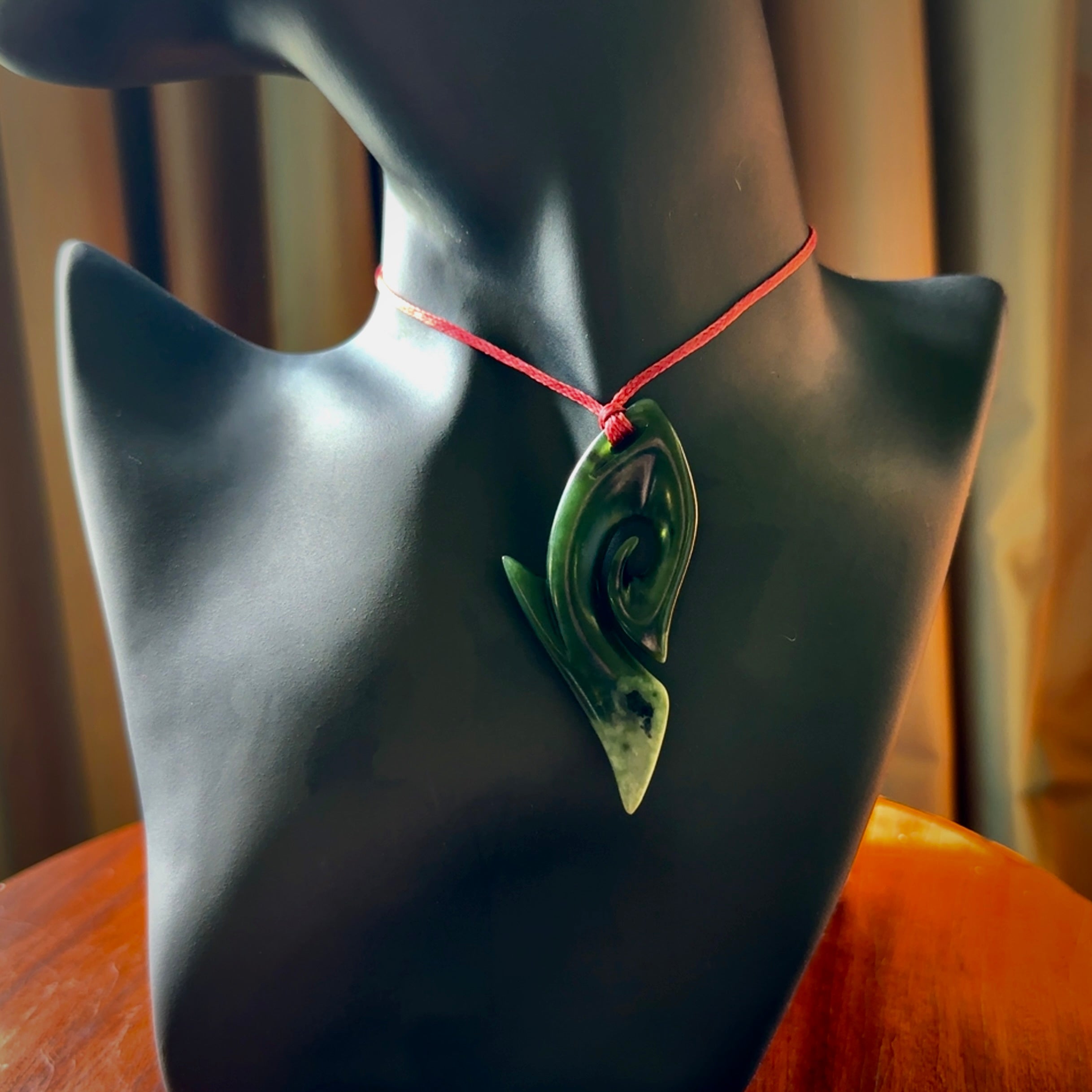 This photo shows a koru pendant carved from New Zealand Jade. The artist, Shaun Gardiner, has carved this beautifully. We provide this piece with an adjustable red cord. This is a fantastic work of art, we have one only.