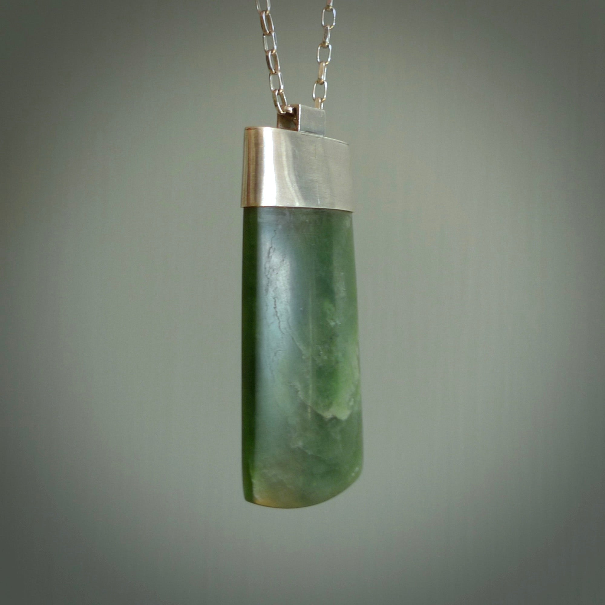 This picture shows a hand carved jade toki, drop pendant with sterling silver cap and chain. The jade is a very dark green with a shimmer in the stone. It is suspended from a sterling silver clasp and we supply a sterling silver chain. Delivery is free worldwide.