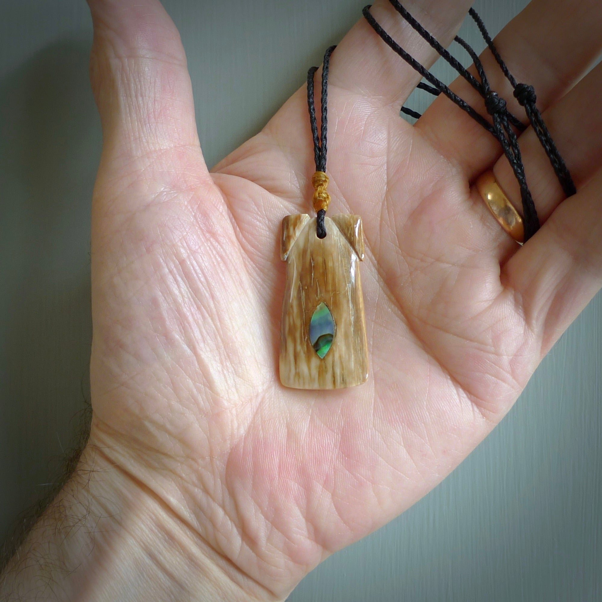 A stunning hand carved Woolly Mammoth Tusk Toki pendant. The toki has a small oval shaped piece of Pāua shell inset into the front face. This piece is bound with an adjustable Black coloured cord. This is a little piece of Art to wear.