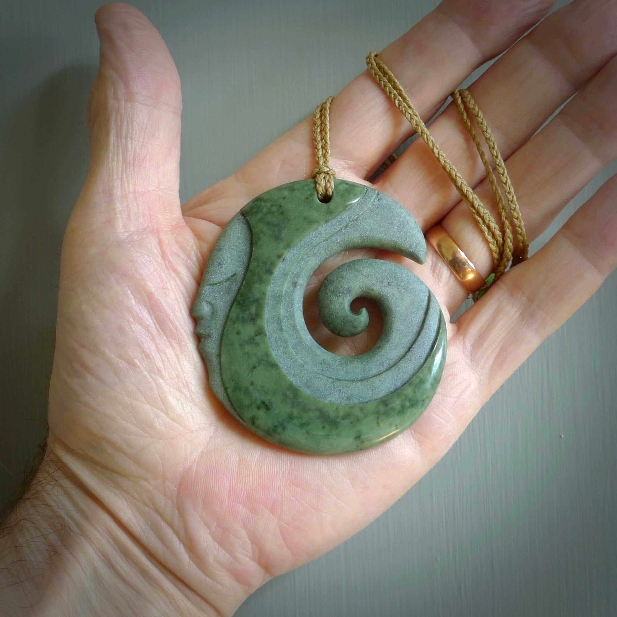 A hand carved koru with face pendant from New Zealand Pounamu, Jade. The cord is Tan and is adjustable. A large hand made Koru necklace by New Zealand artist Kerry Thompson.