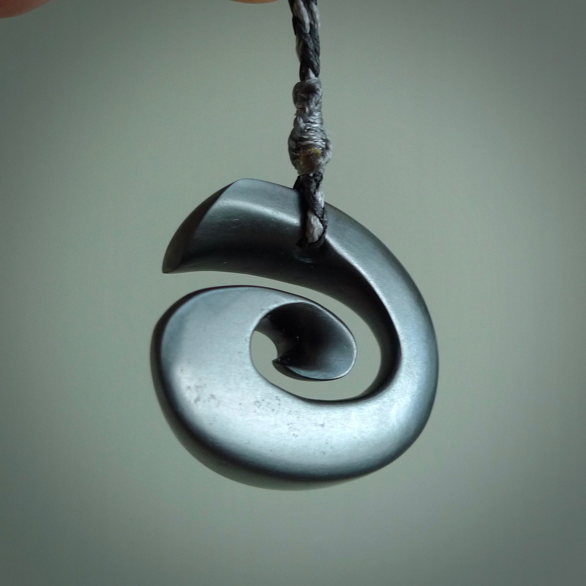 A hand carved medium sized Black Jade Koru necklace. The cord is a black colour and is a fixed length . A medium sized hand made hook necklace by New Zealand artist Kerry Thompson. One off work of art to wear.