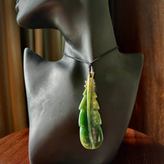 Hand carved New Zealand Marsden Jade feather pendant. Made by Ana Krakosky for NZ Pacific in New Zealand Pounamu, jade. A beautiful dark green and orange jade feather drop necklace with black adjustable cord.