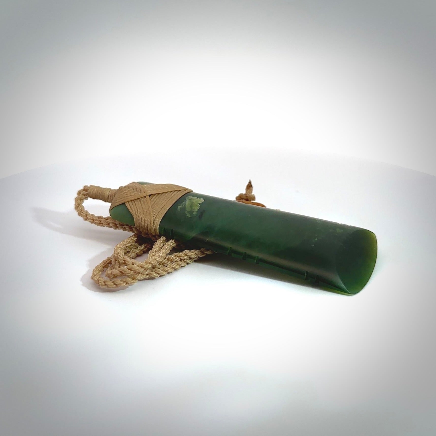 A large and beautiful hand carved toki pendant. This piece is carved from New Zealand jade by Jeromy Van Riel. This is a wonderful large toki bound with a hand-plaited cord and a traditional lashing. A beautiful, traditional toki for sale online.