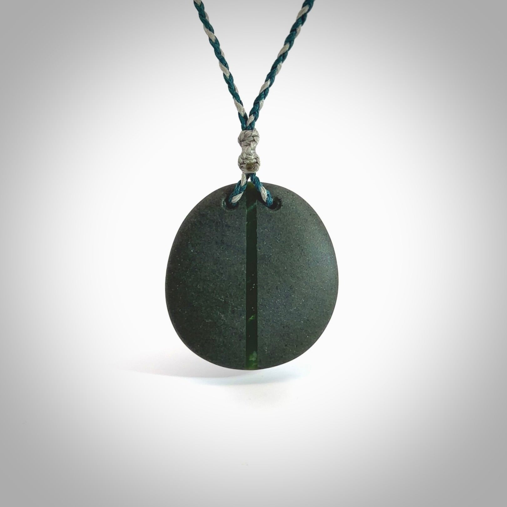 Greywacke stone pendant with New Zealand Jade Pounamu insert. Hand carved by Rhys Hall for NZ Pacific. Handmade jewellery for sale online. Delivered to you with express courier in one of our kete pouches.