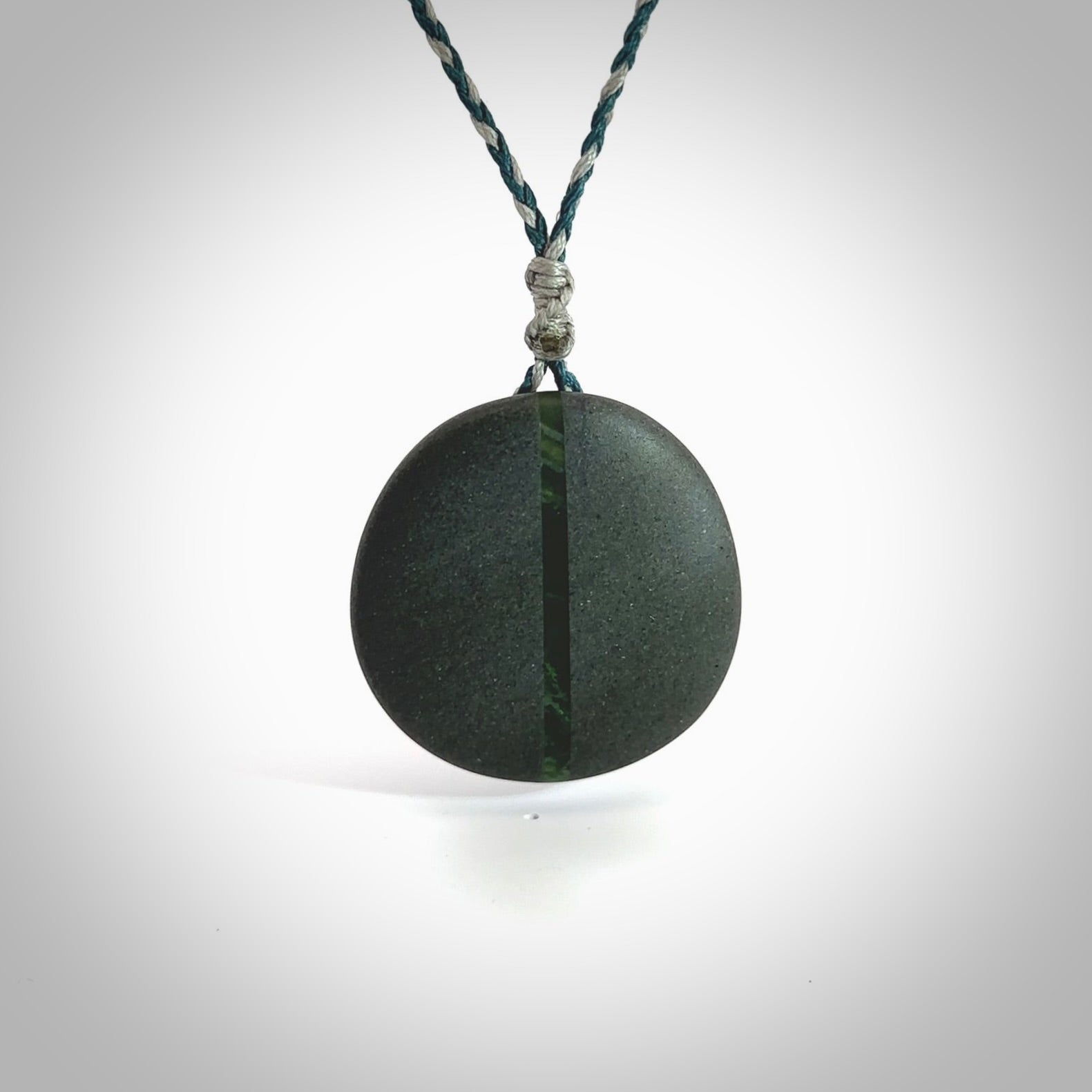 Greywacke stone pendant with New Zealand Jade Pounamu insert. Hand carved by Rhys Hall for NZ Pacific. Handmade jewellery for sale online. Delivered to you with express courier in one of our kete pouches.