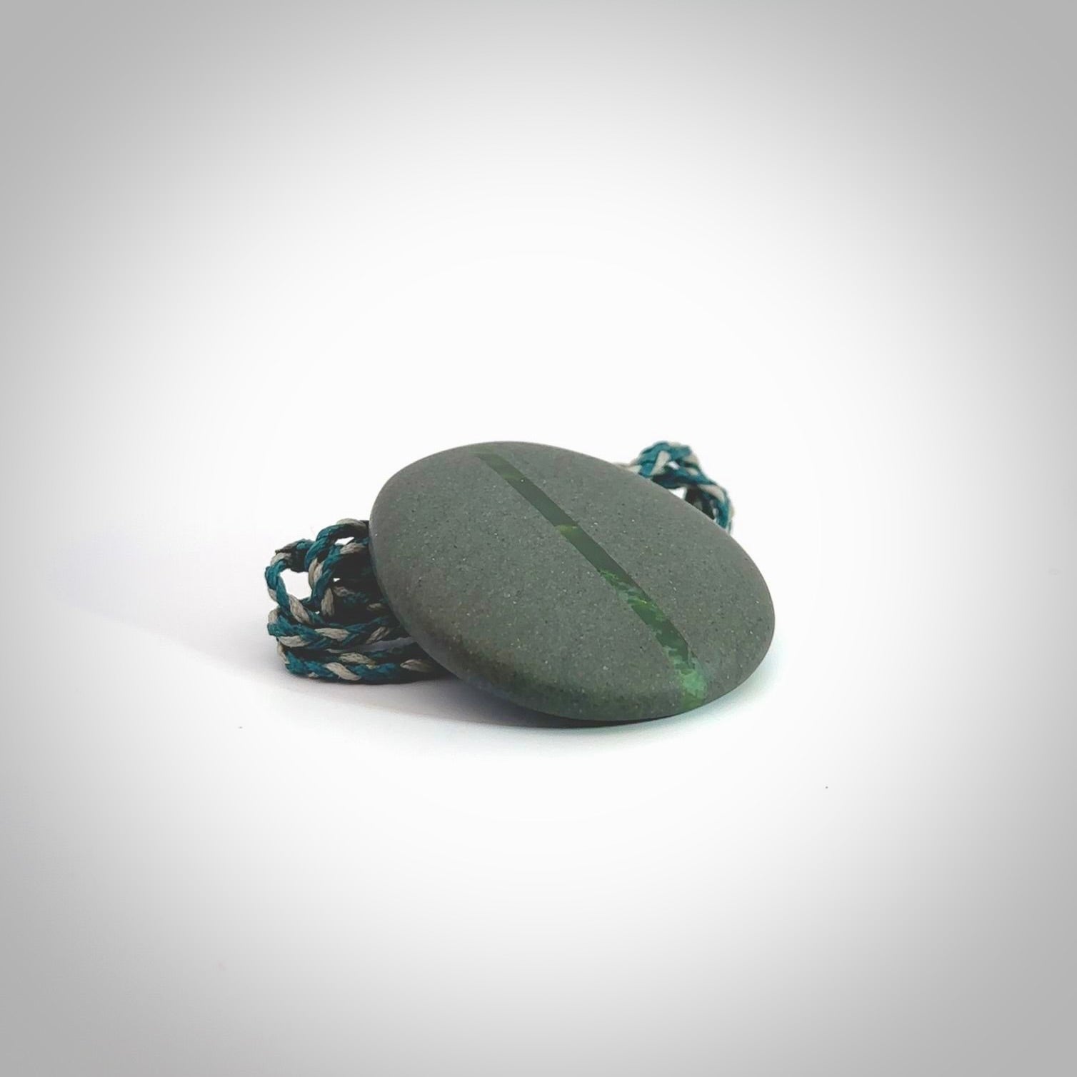 Greywacke stone pendant with New Zealand Jade Pounamu insert. Hand carved by Rhys Hall for NZ Pacific. Handmade jewellery for sale online. Delivered to you with express courier in one of our kete pouches.