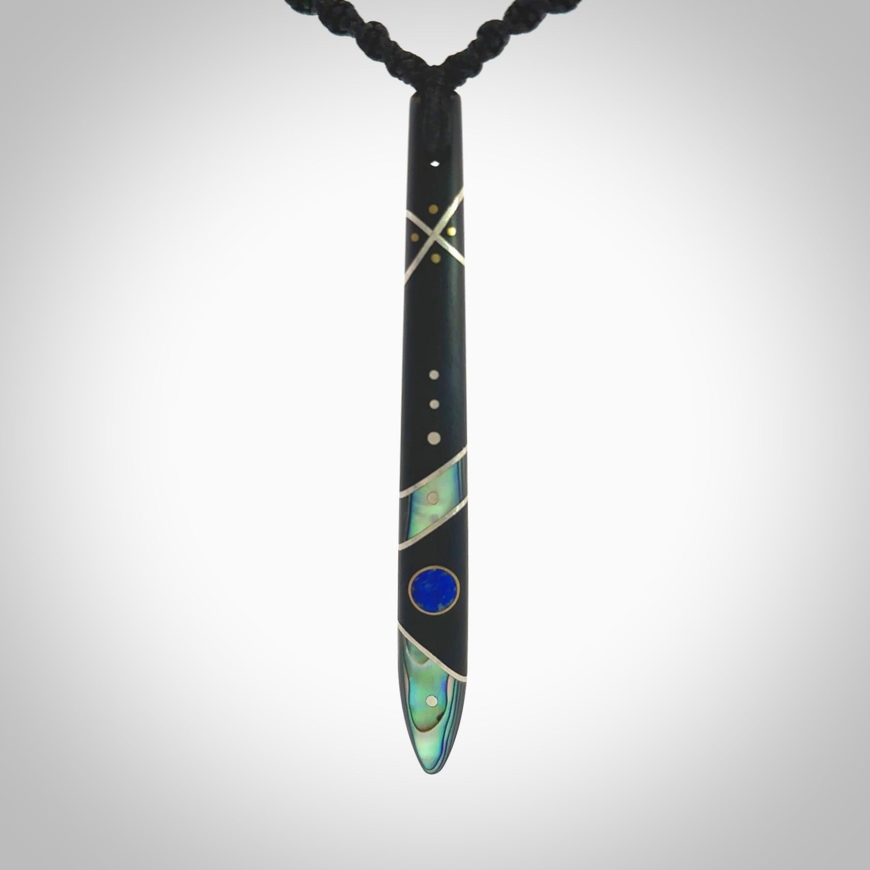 This photo shows a medium sized taiaha pendant hand carved from piano key with Afghani Lapis Lazuli and Chinese Glowing Stone, Sleeping Beauty Turquoise inlay alongside; brass and silver. This is a stand out one off necklace for those who appreciate art to wear. It is provided with a cord in black that is a fixed length with Paua Shell Toggle. We ship this piece worldwide and shipping is included in the price.