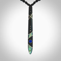 This photo shows a medium sized taiaha pendant hand carved from piano key with Afghani Lapis Lazuli and Chinese Glowing Stone, Sleeping Beauty Turquoise inlay alongside; brass and silver. This is a stand out one off necklace for those who appreciate art to wear. It is provided with a cord in black that is a fixed length with Paua Shell Toggle. We ship this piece worldwide and shipping is included in the price.