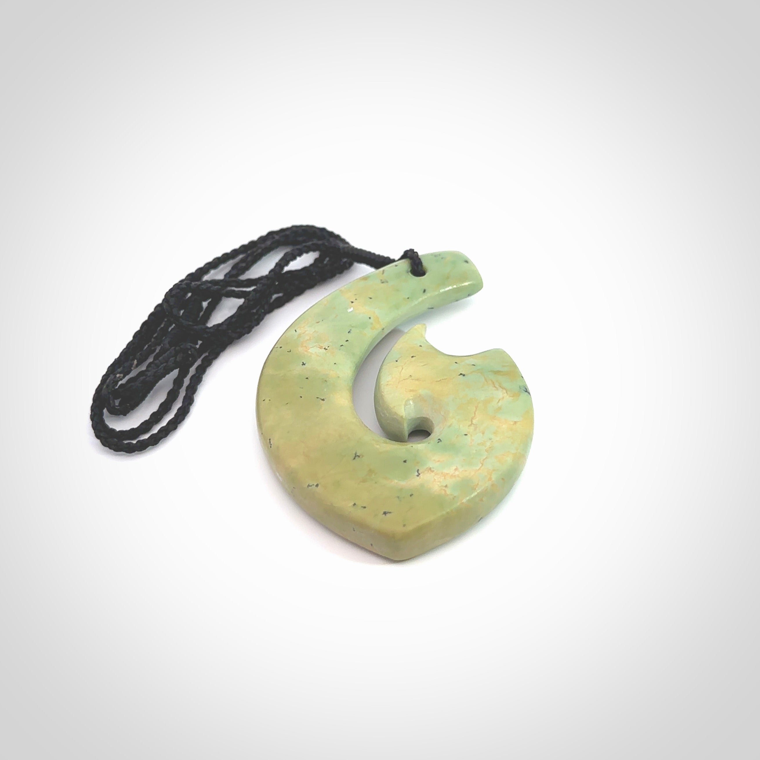 This picture shows a carved Matau, Hook, in New Zealand Jade. It is a hook shaped pendant pendant that culminates in a fish tail. It is provided with a black coloured cord that is length adjustable. Hand made in New Zealand by Andrew Doughty.