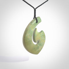 This picture shows a carved Matau, Hook, in New Zealand Jade. It is a hook shaped pendant pendant that culminates in a fish tail. It is provided with a black coloured cord that is length adjustable. Hand made in New Zealand by Andrew Doughty.