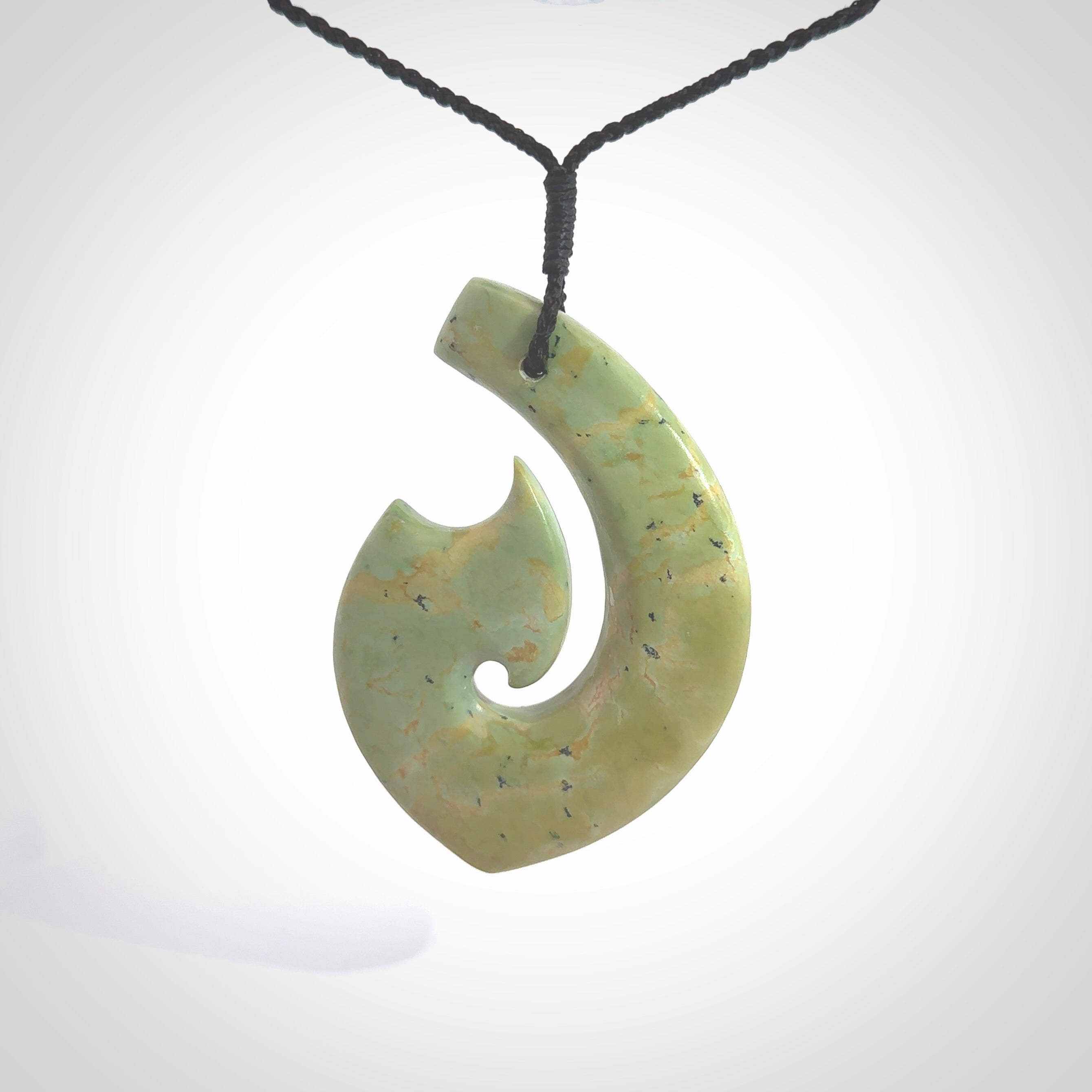 This picture shows a carved Matau, Hook, in New Zealand Jade. It is a hook shaped pendant pendant that culminates in a fish tail. It is provided with a black coloured cord that is length adjustable. Hand made in New Zealand by Andrew Doughty.