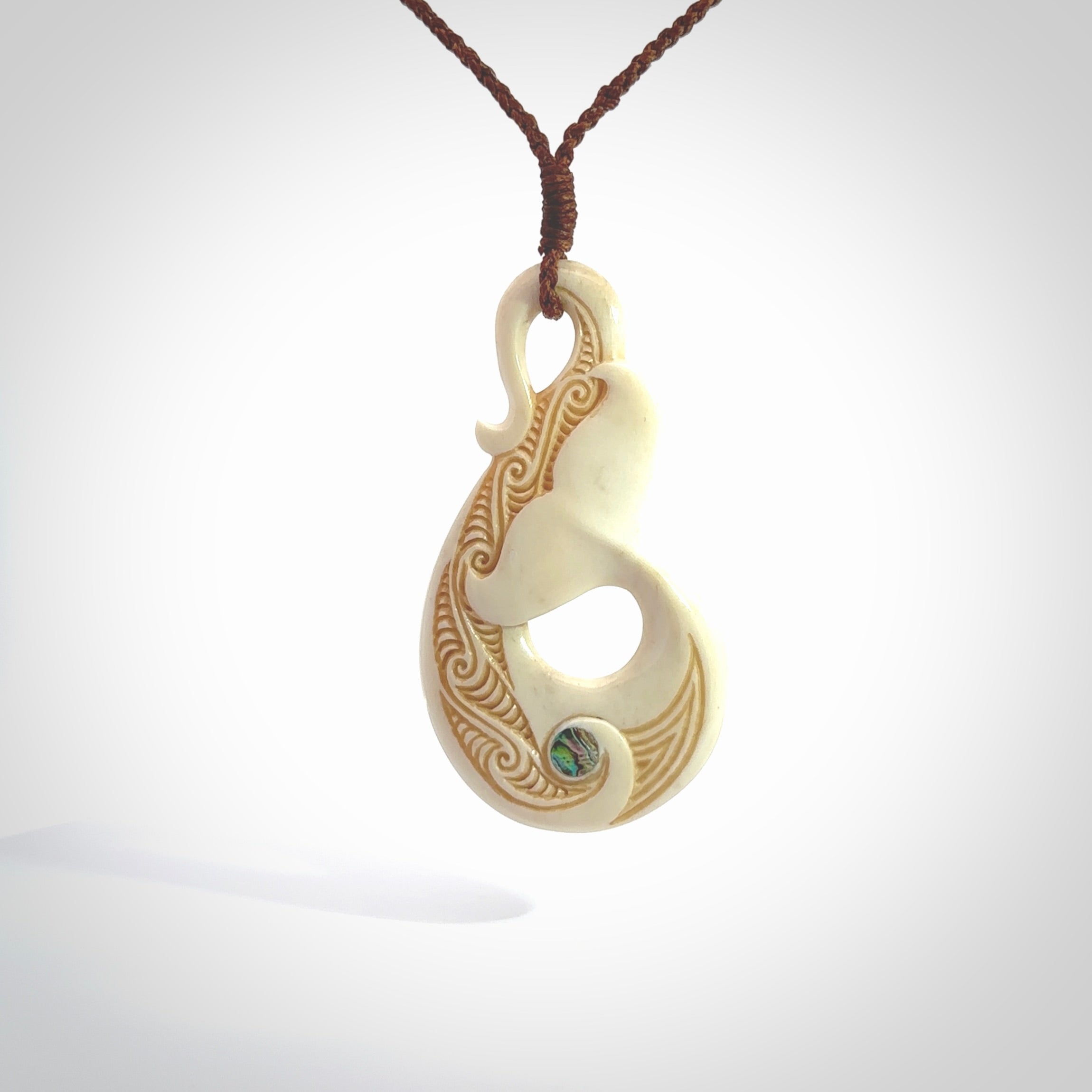 Hand carved Bone Whale Tail pendant with Paua shell inlay by Andrew Doughty. Whale tail pendant by Andrew Doughty with engraving in it. Beautiful unisex necklace hand carved in New Zealand, delivered in a woven kete pouch. Provided with an adjustable brown cord.