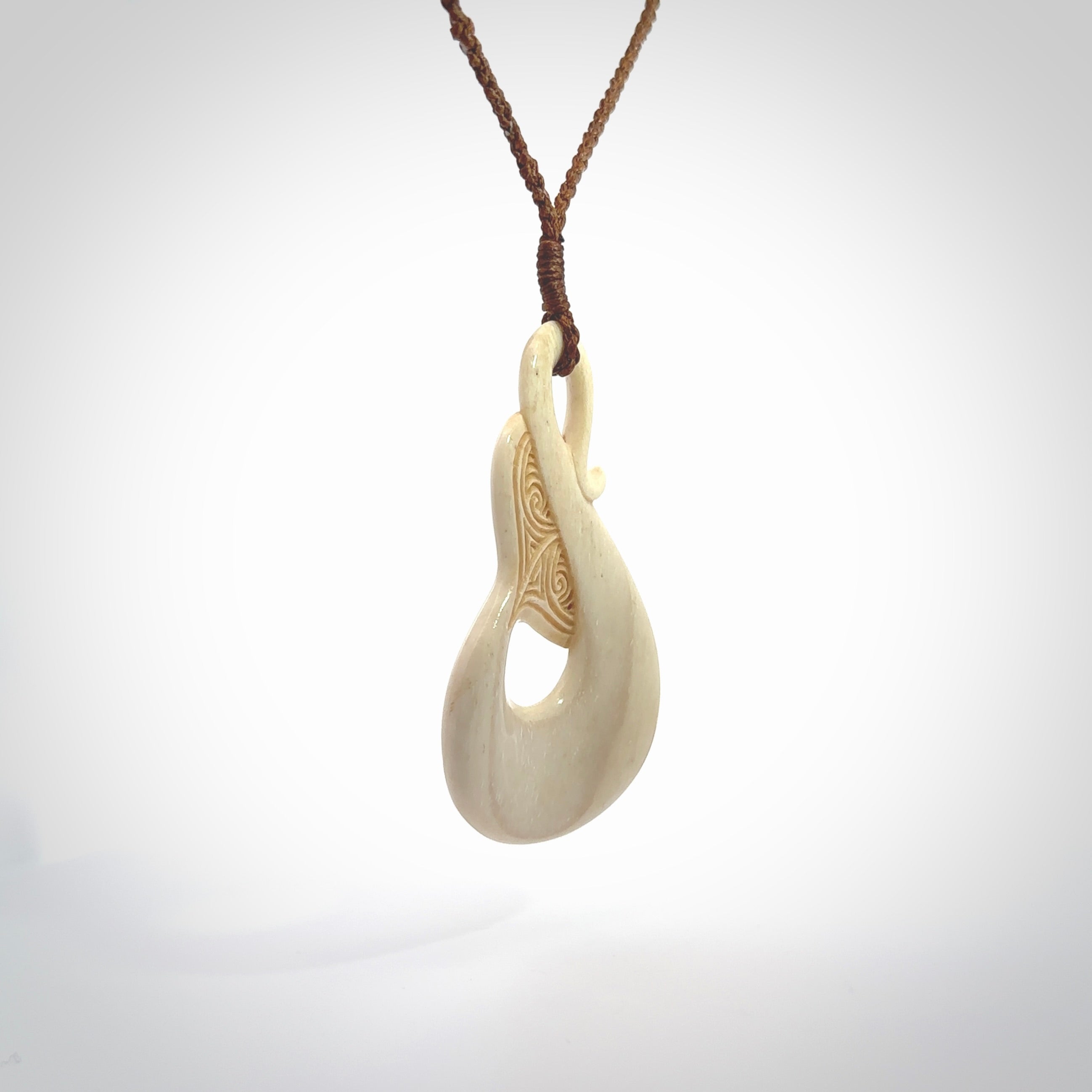 Hand carved Bone Whale Tail pendant with Paua shell inlay by Andrew Doughty. Whale tail pendant by Andrew Doughty with engraving in it. Beautiful unisex necklace hand carved in New Zealand, delivered in a woven kete pouch. Provided with an adjustable brown cord.