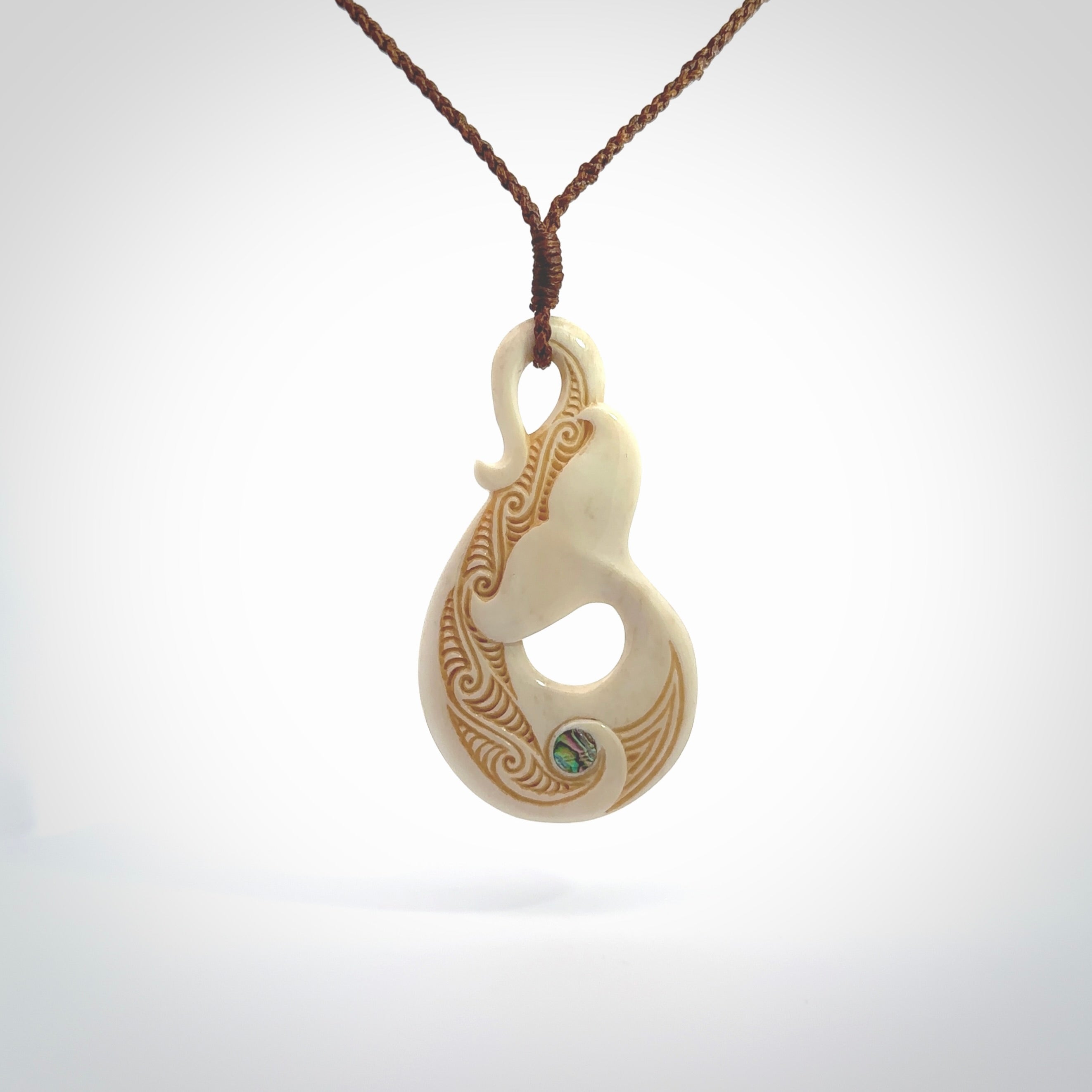 Hand carved Bone Whale Tail pendant with Paua shell inlay by Andrew Doughty. Whale tail pendant by Andrew Doughty with engraving in it. Beautiful unisex necklace hand carved in New Zealand, delivered in a woven kete pouch. Provided with an adjustable brown cord.