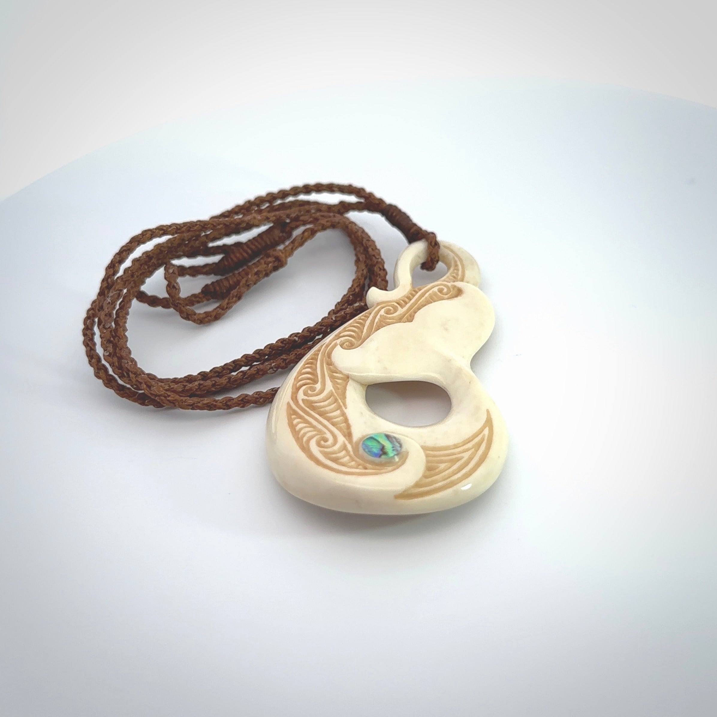 Hand carved Bone Whale Tail pendant with Paua shell inlay by Andrew Doughty. Whale tail pendant by Andrew Doughty with engraving in it. Beautiful unisex necklace hand carved in New Zealand, delivered in a woven kete pouch. Provided with an adjustable brown cord.