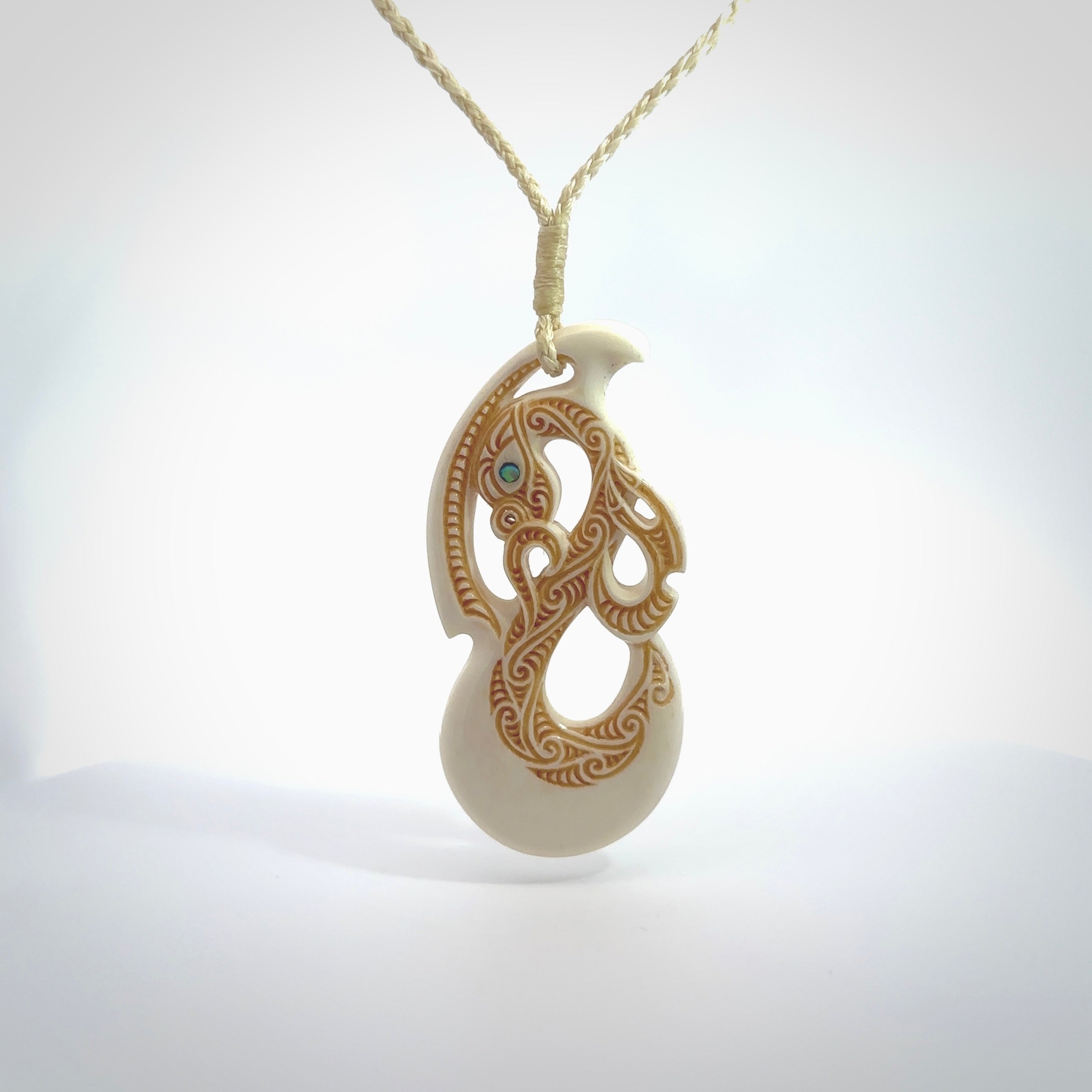 This picture shows a carved manaia in bone. The artist has carved traditional decorative kowhaiwhai designs into the body and these run up the insides of the manaia. These have specific meanings. It is provided with a hand-plaited beige cord that is length adjustable. Free shipping worldwide.